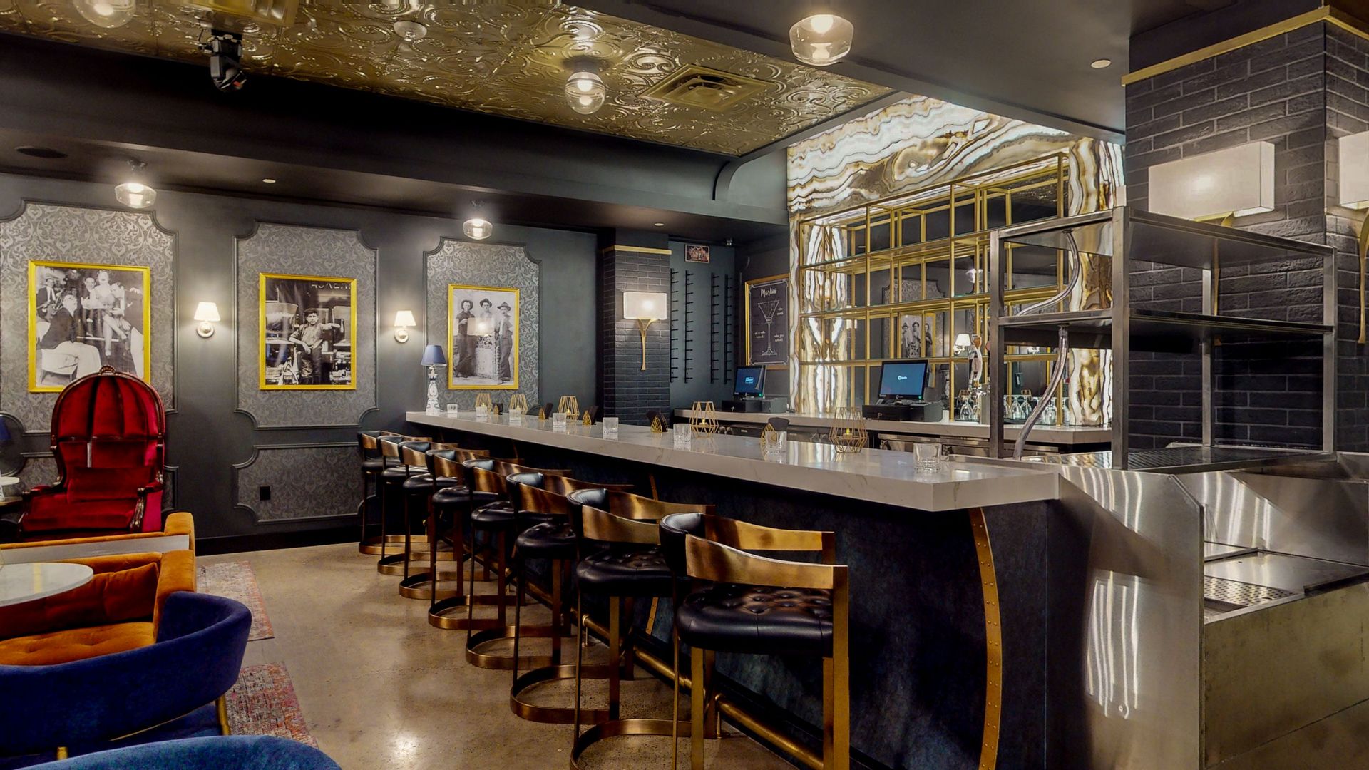 A luxury bar with black walls, gold accents, and a long counter with stools; a mirror and photos are visible.