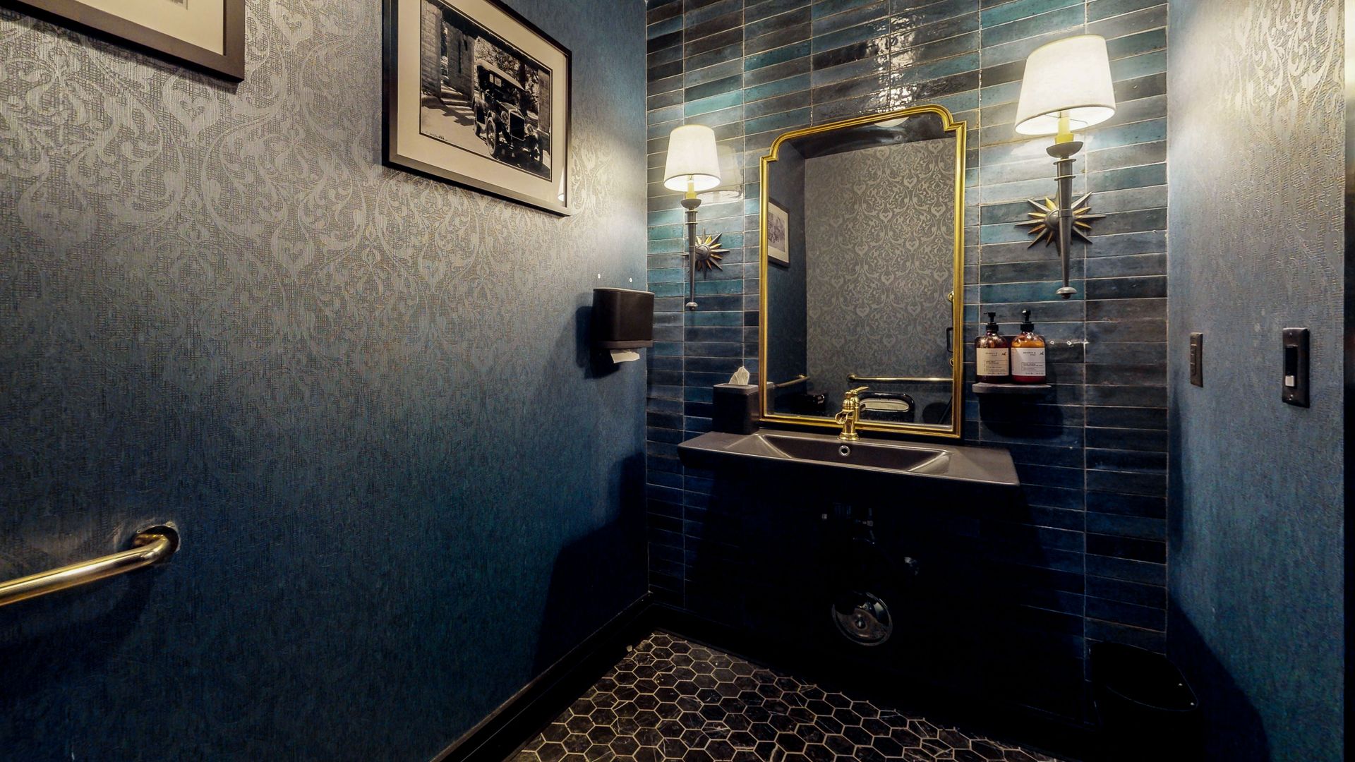 A dark blue bathroom with gold accents, a black sink, and a decorative mirror.