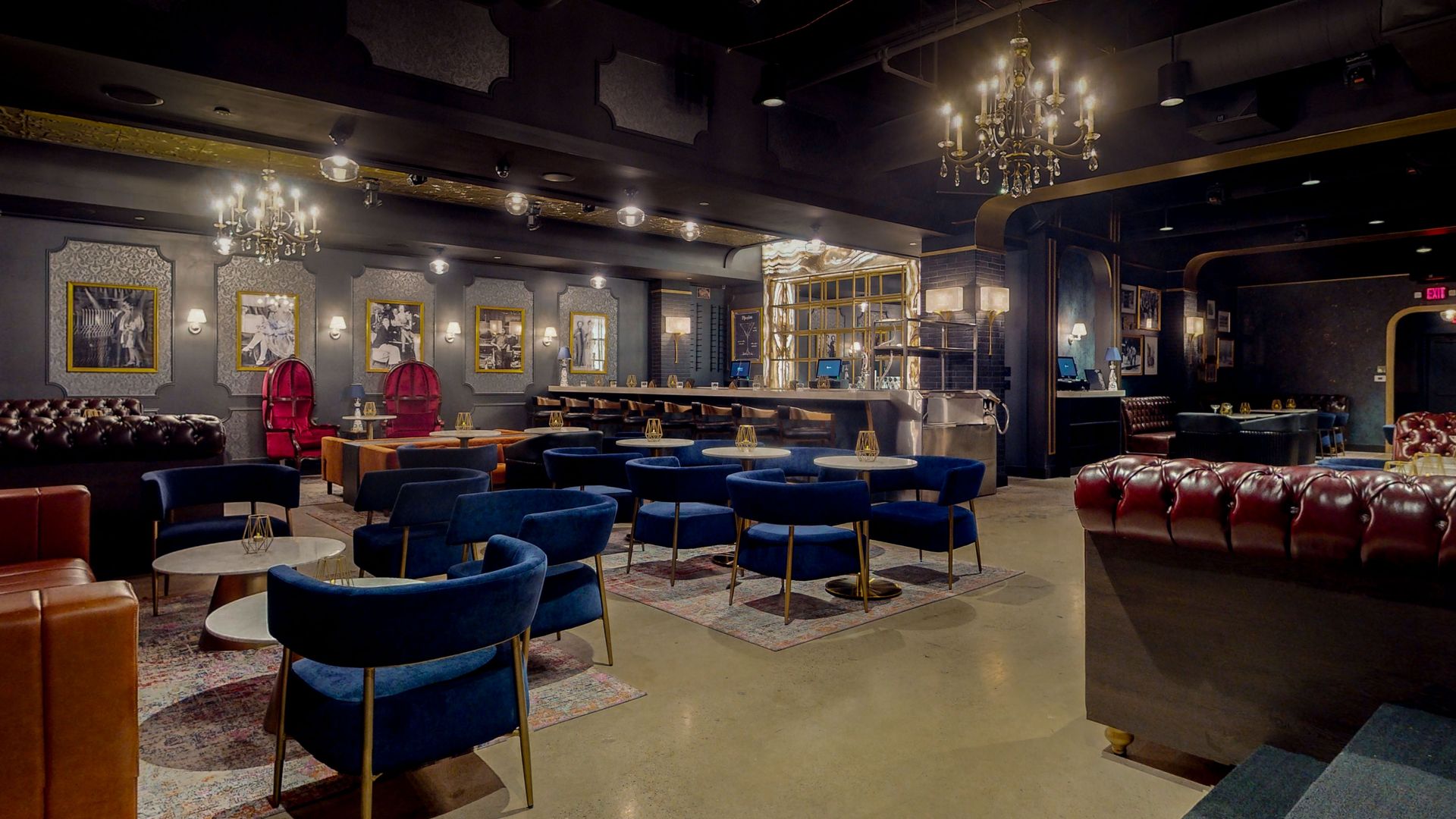 Elegant bar interior with blue velvet chairs, a bar, and chandeliers.