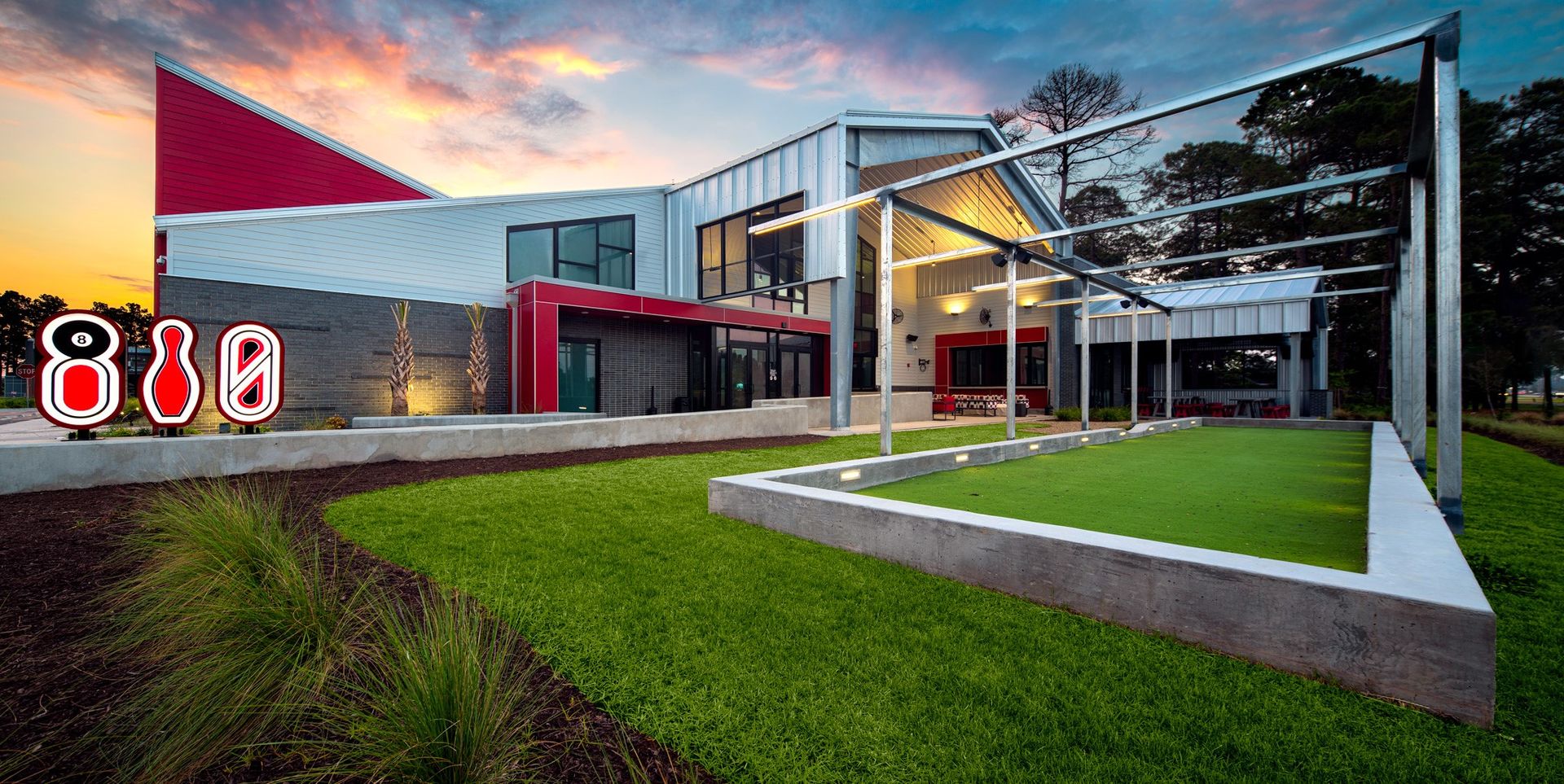 Modern building with a red angled roof and lawn with signage shaped like a bowling ball, pin and bowling lane.