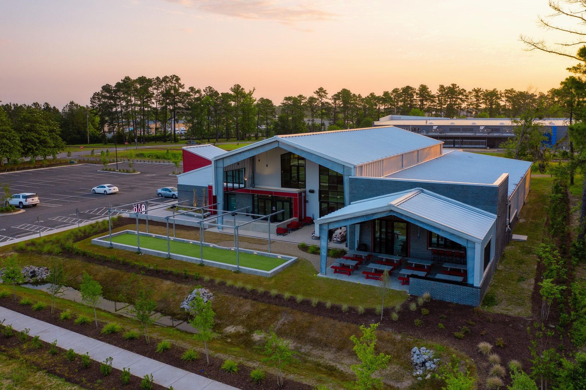 Modern building with red and gray accents, outdoor seating, and parking area.