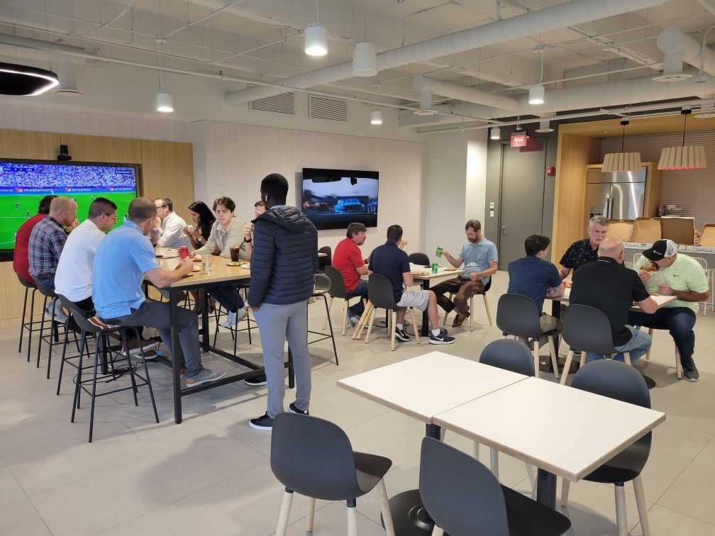 People gathered around tables in a bright office lounge for a meeting or event.