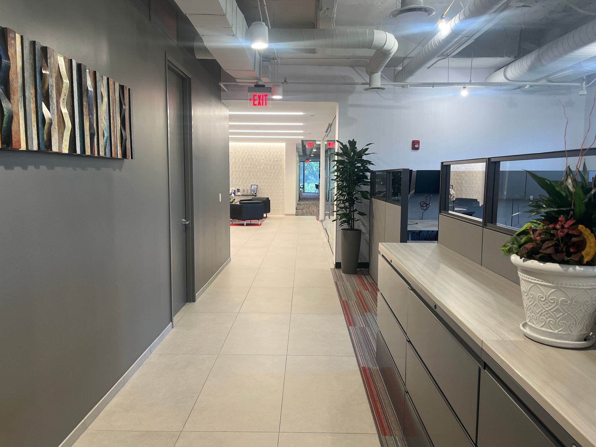 Office hallway with gray walls, tiled floor, desk, and a potted plant near a bright doorway