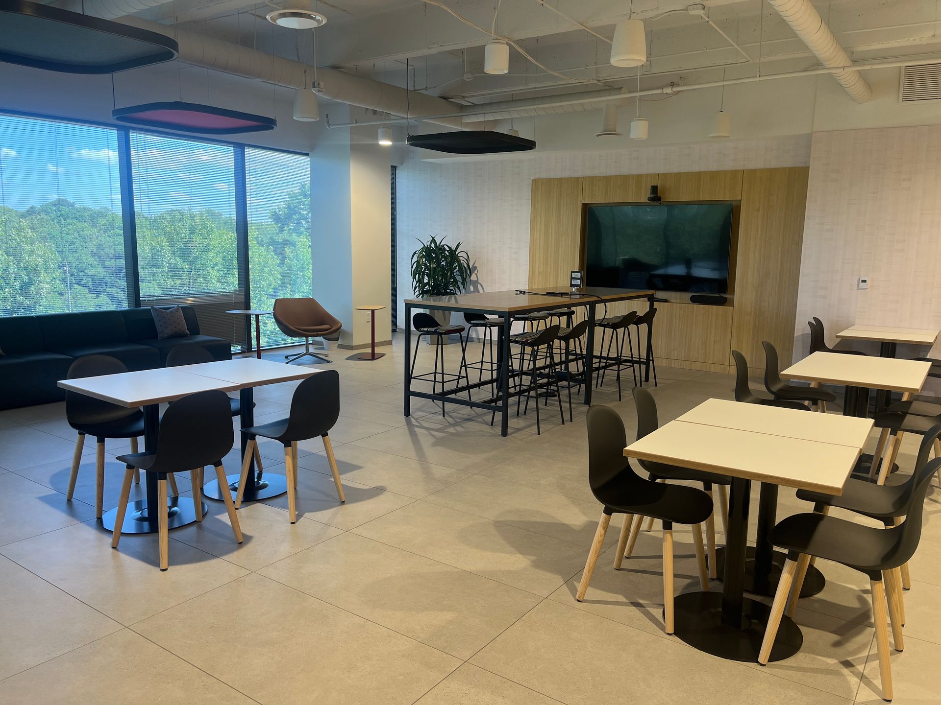 Modern lounge with tables, chairs, large windows, and a TV mounted on a wood-paneled wall.