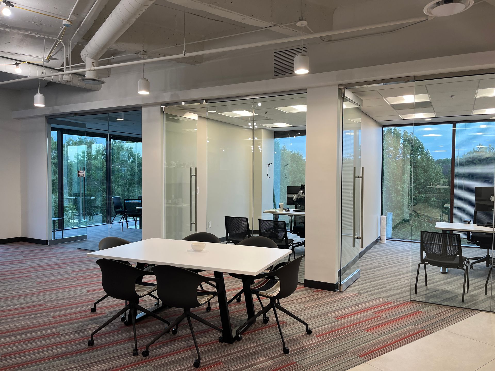 Modern office with glass-walled meeting rooms, tables, chairs, and carpeted open workspace.