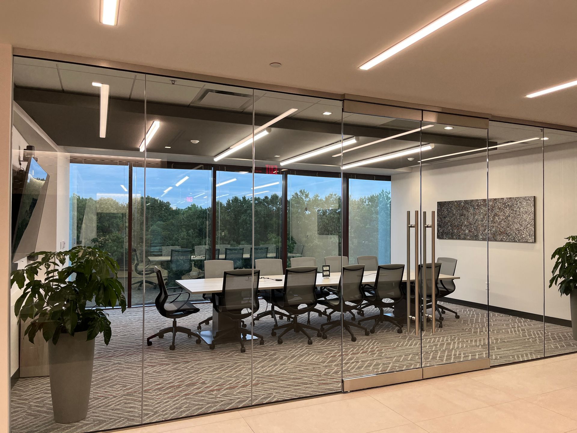 Modern glass conference room with oval table, black chairs, and city view through large windows