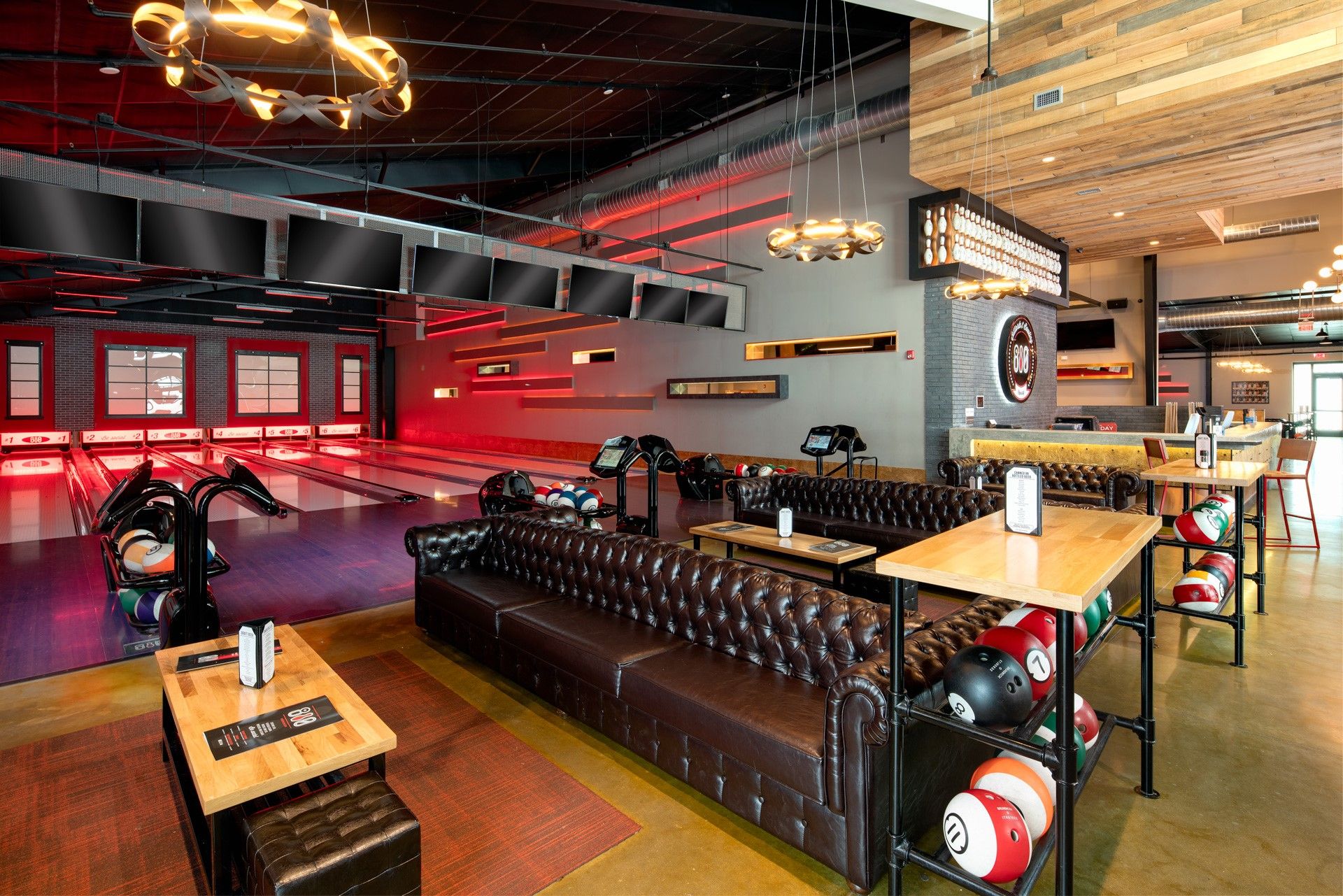 Bowling alley interior: leather couches, bowling balls on display, red and gray walls, overhead TVs.