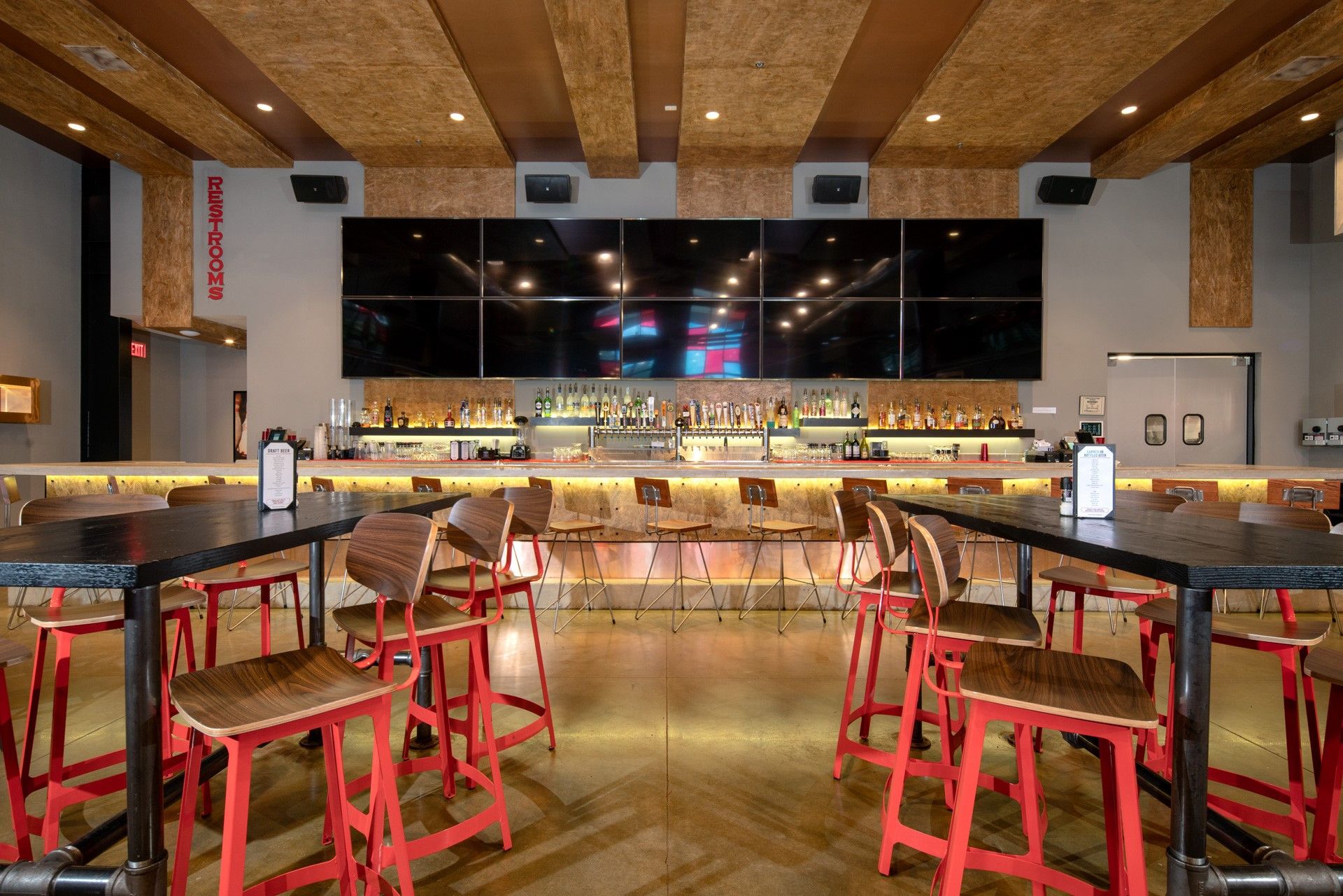 Bar interior: red chairs, black tables, a long bar with drinks, and multiple TVs.