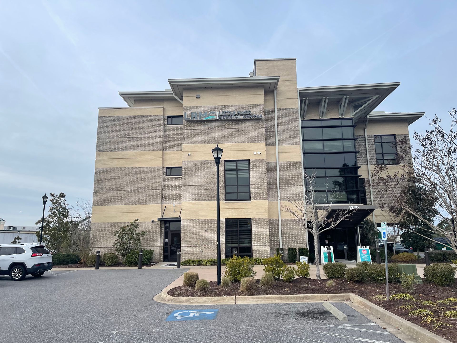 Exterior view of a two-story brick building with glass windows. Parking spots, including a handicap spot, are in front.