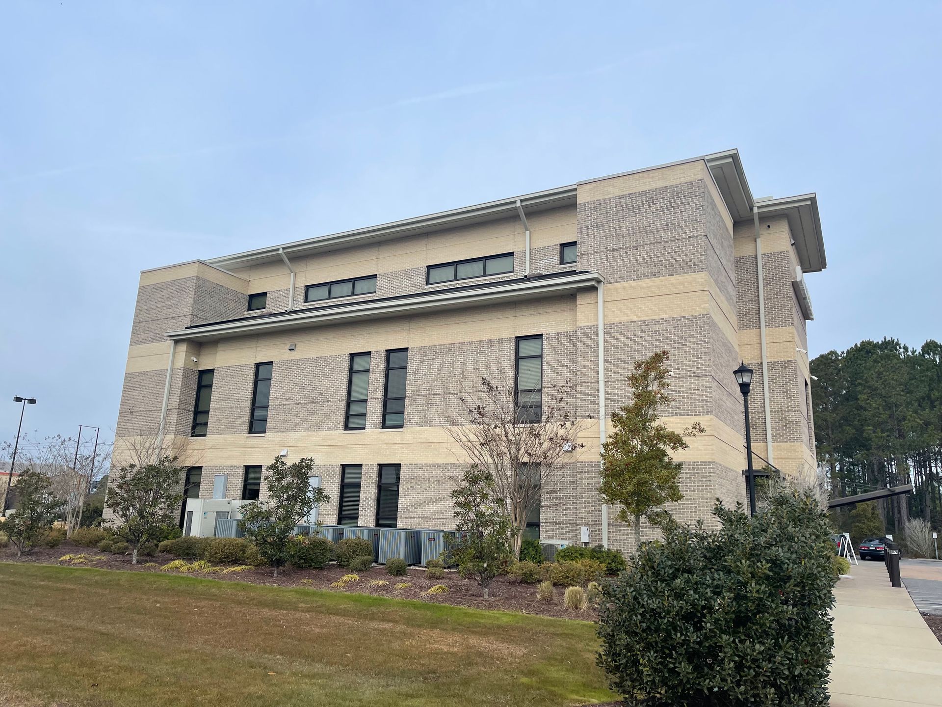 Modern brick building with dark windows on a cloudy day. Green shrubbery and trees in the foreground.