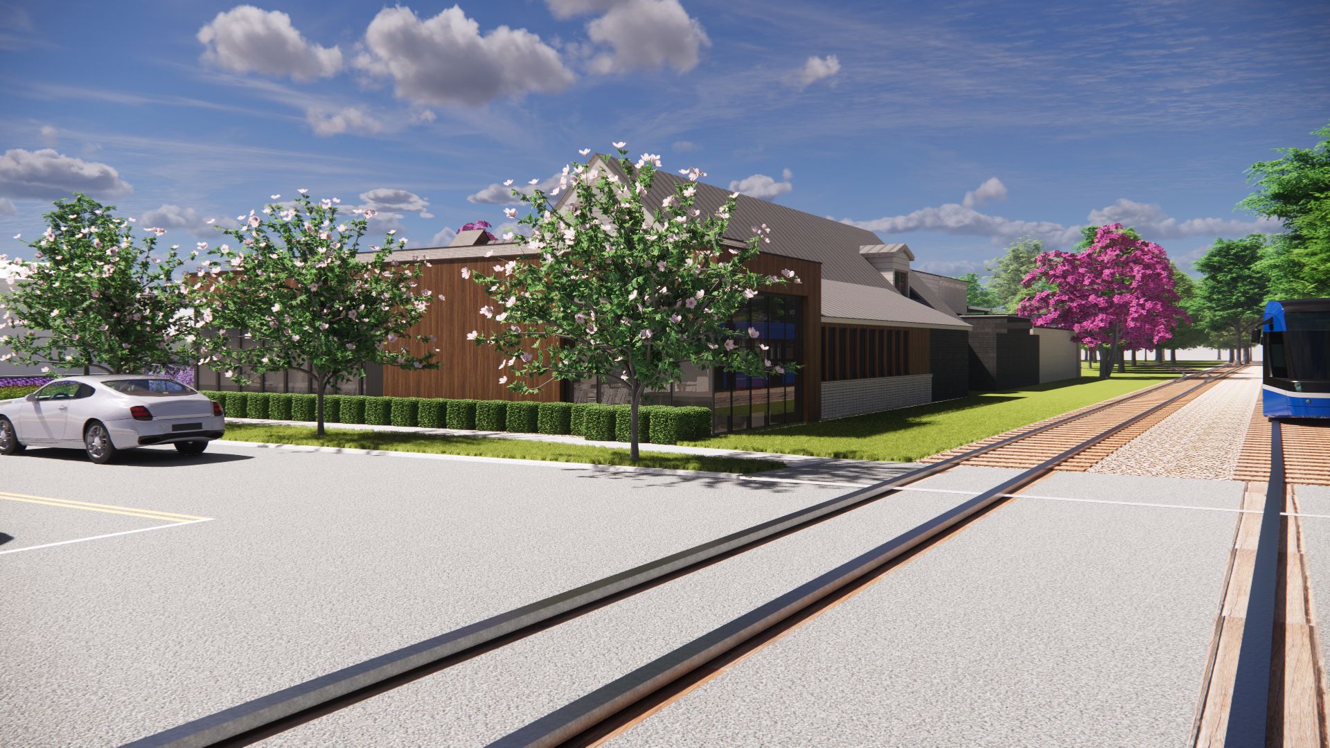 Street view of building with car, trees, and train tracks on a bright day.