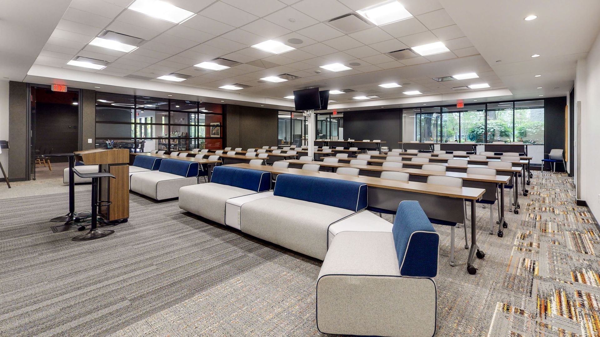 Empty modern conference room with rows of tables, blue sofas, and bright ceiling lights