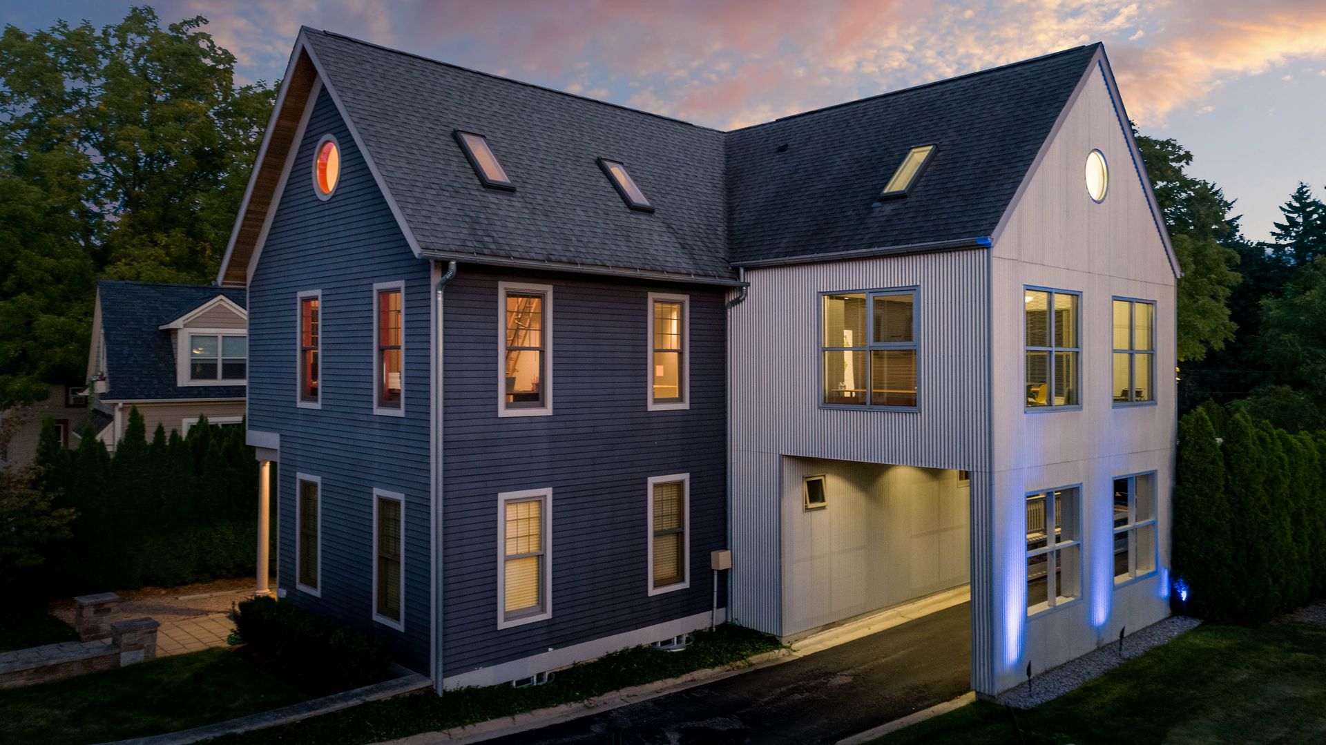 Two-story modern home with gray and white siding, multiple windows, and an open breezeway.
