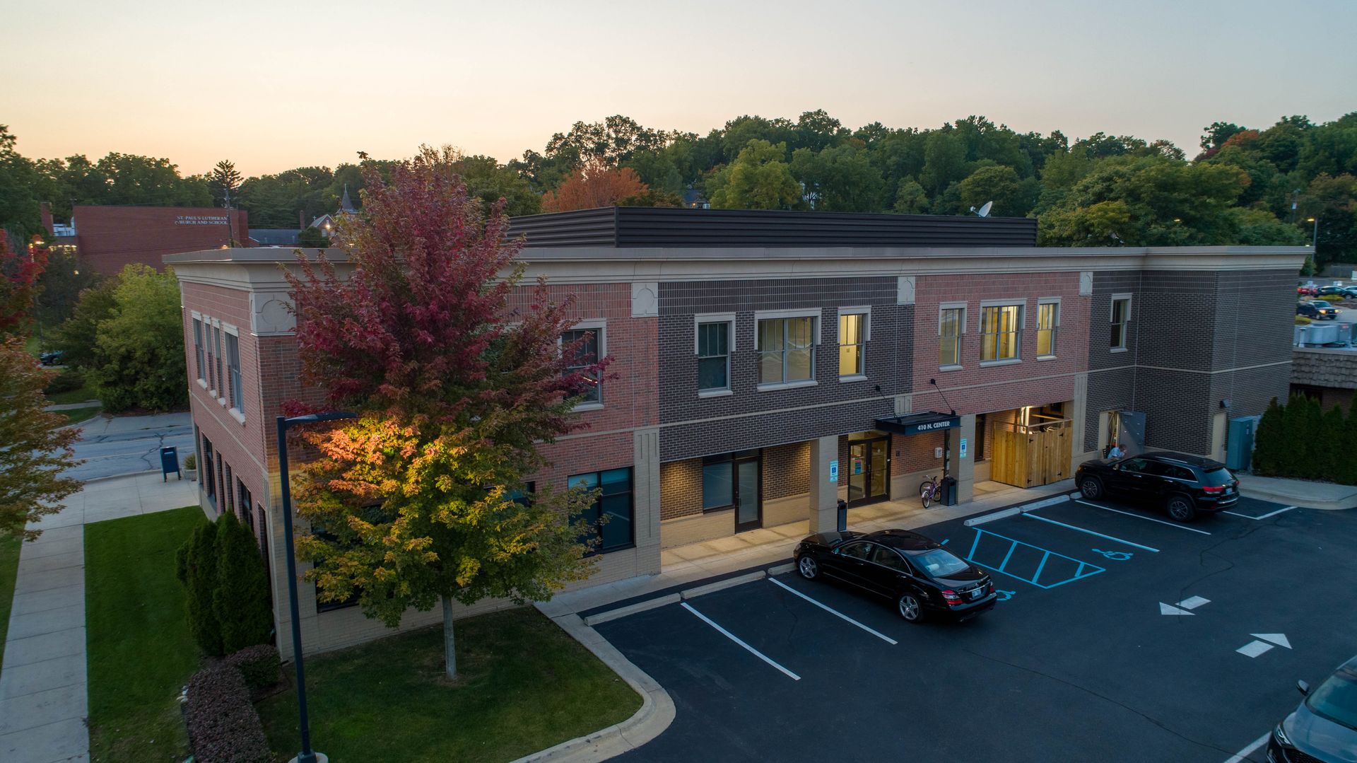 Two-story brick building with parking; trees with fall colors, dusk sky.