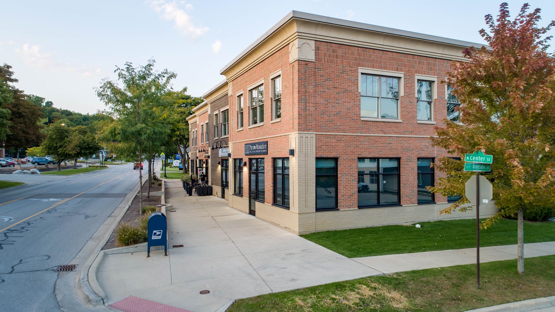 Brick building on a corner with a sidewalk, street, and trees; blue mailbox in front.