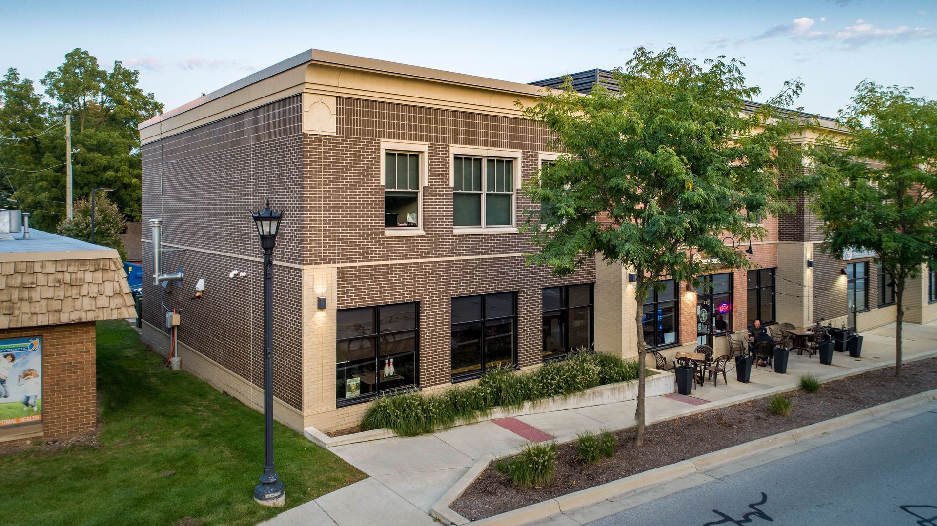 Two-story brick building with large windows, sidewalk seating, and a streetlamp in front.