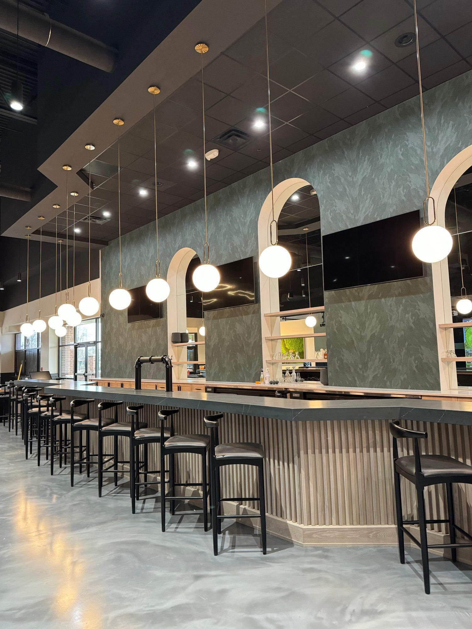 Bar with tall black stools, hanging globe lights, and teal textured wall.