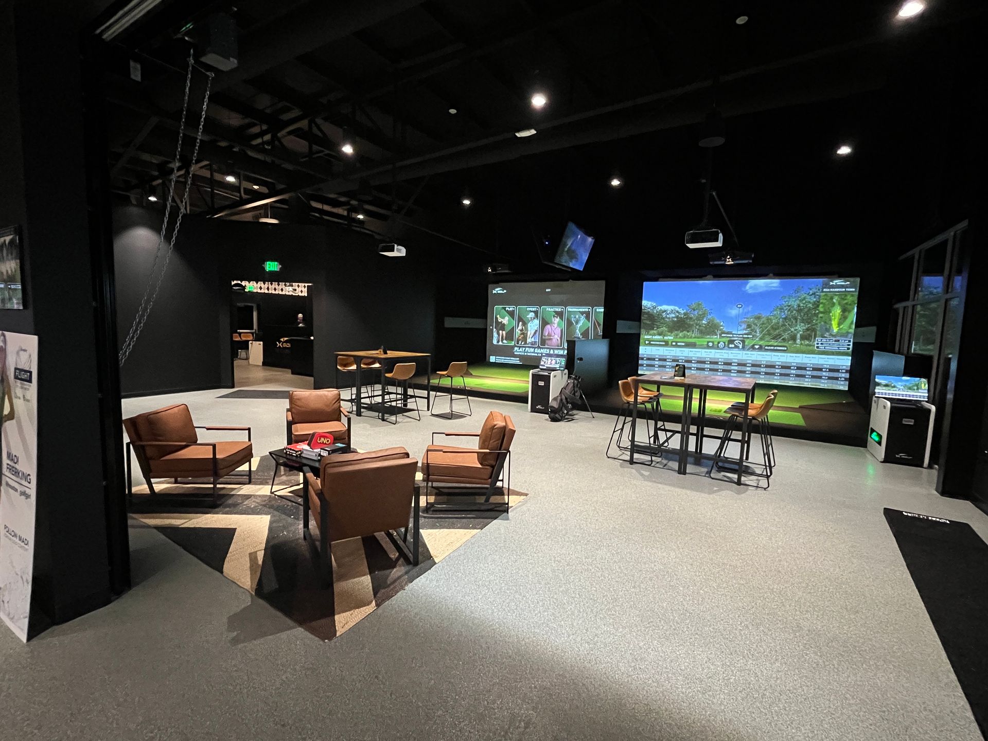 An indoor golf simulator with screens, seating, and a dark color scheme.