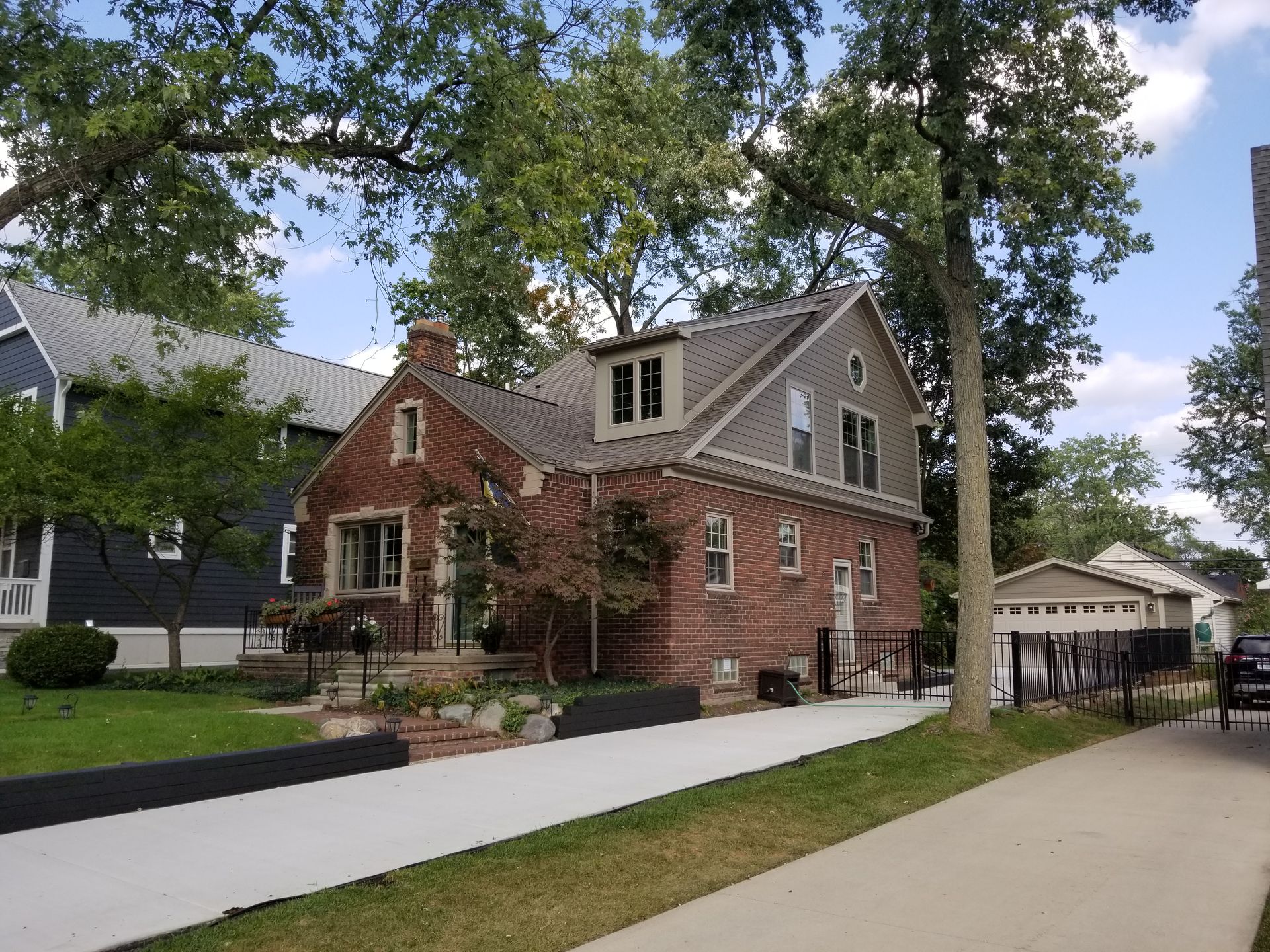 Brick house with a gray roof and dormer, a driveway, and trees in a residential neighborhood.