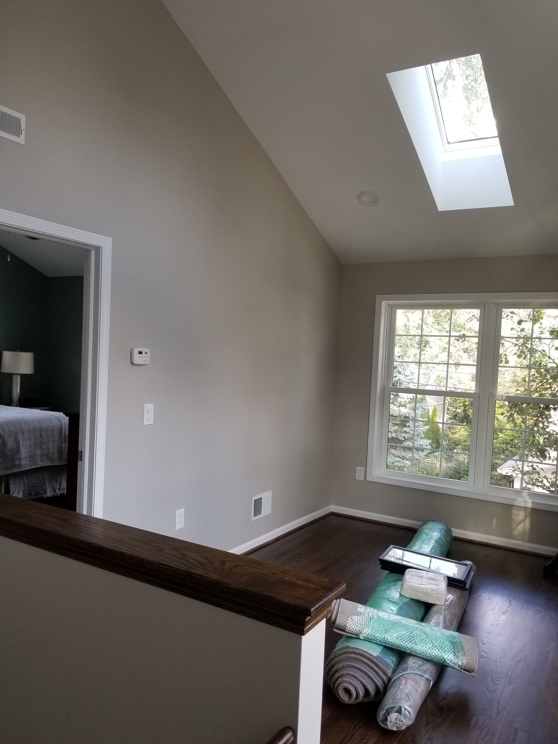 Interior view of a landing with a window and skylight. Rolled rugs are on the floor, leading to a bedroom doorway.