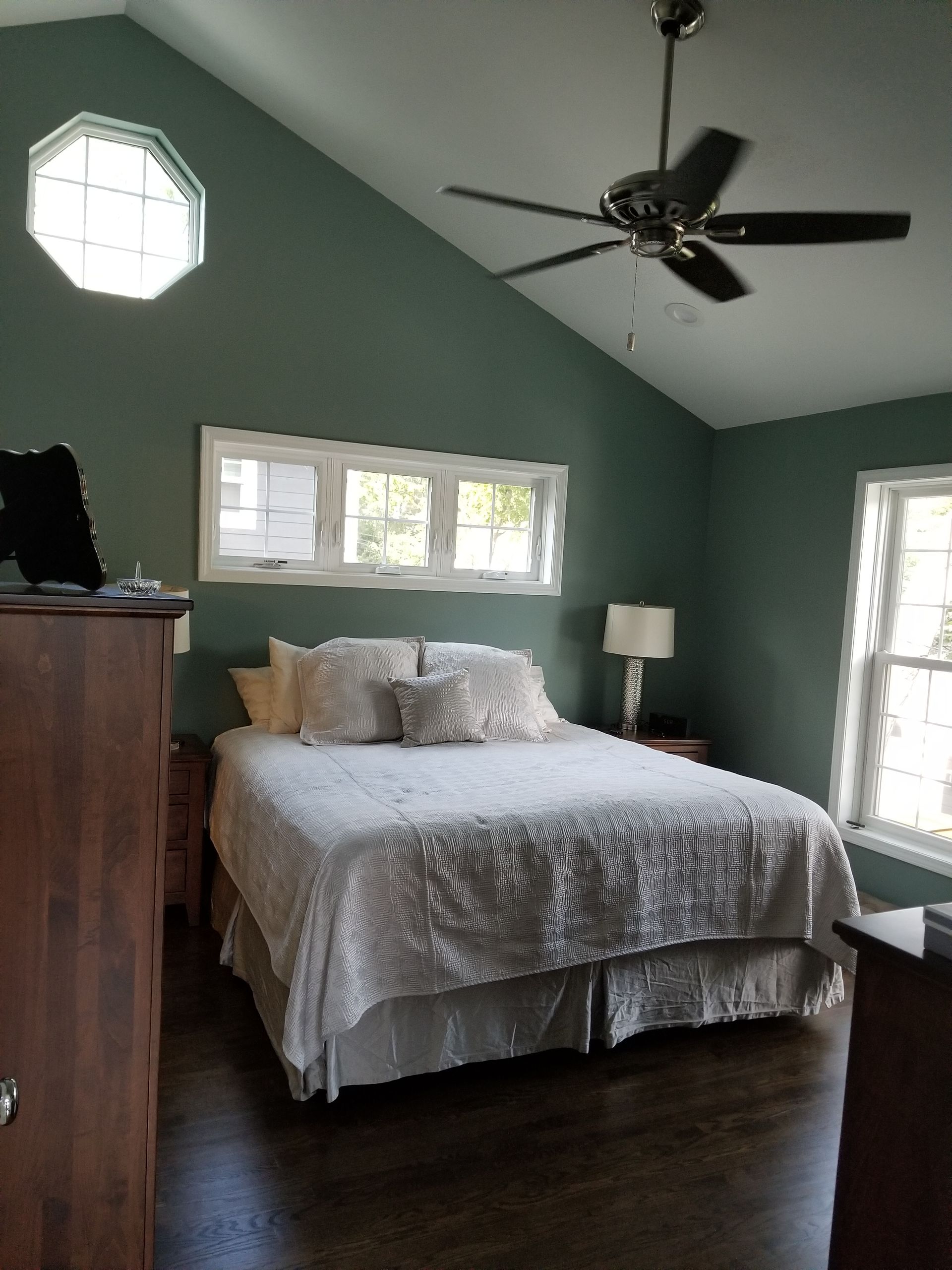 Bedroom with a bed, windows, and ceiling fan, green walls, and wooden furniture.