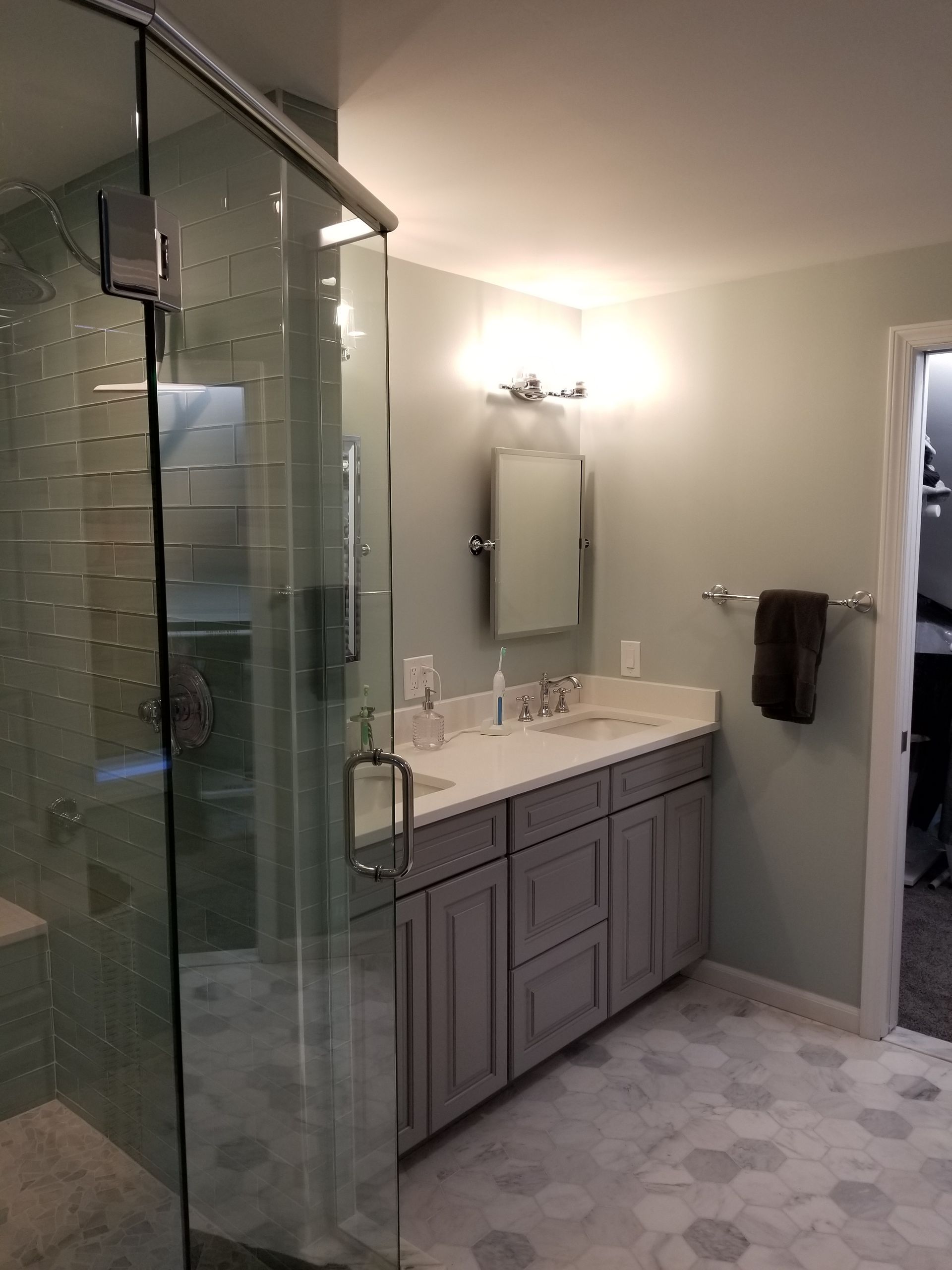 Bathroom with glass shower, grey vanity, hexagonal floor tiles, and a light blue wall.