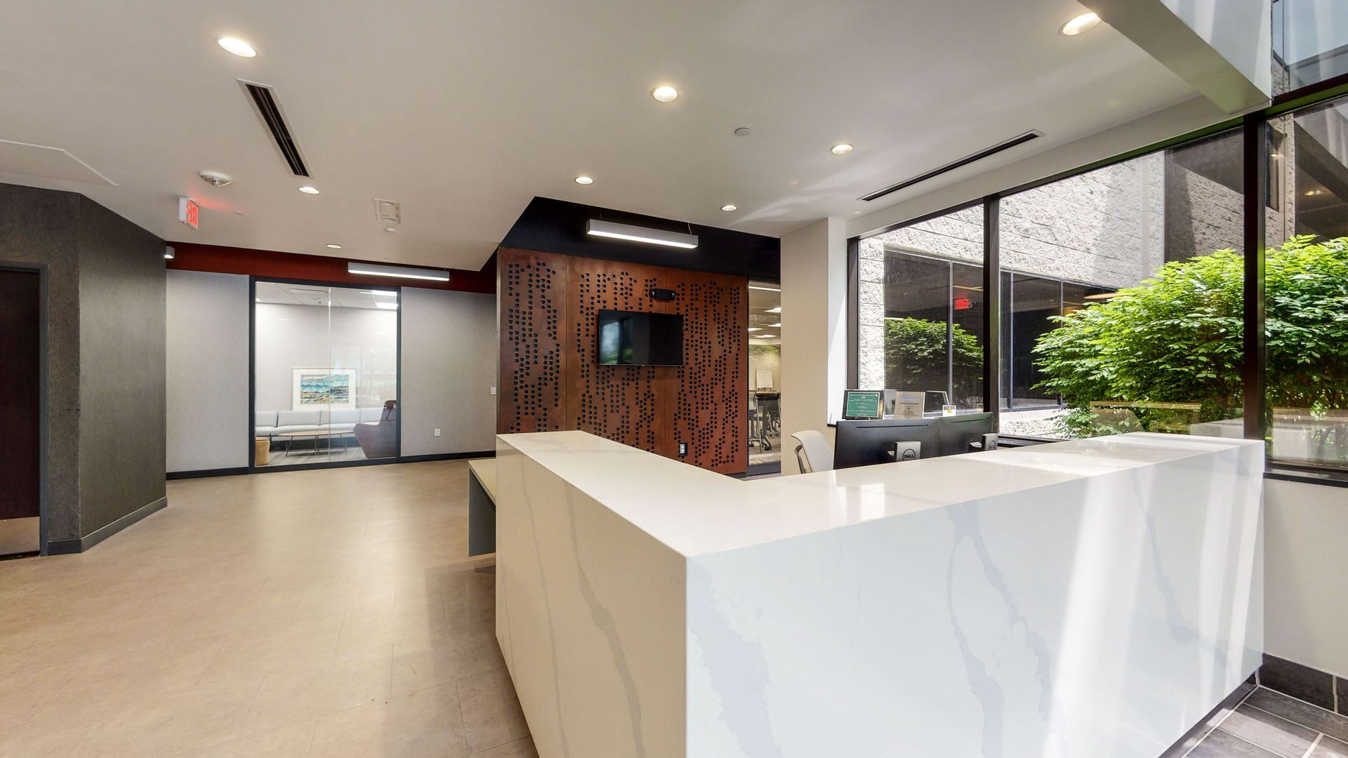 Modern office lobby with white reception desk, wood accent wall, and large windows overlooking greenery.
