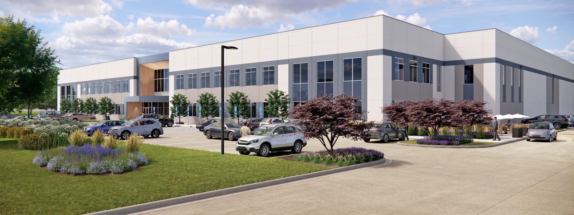 Modern industrial building with cars parked in front, a landscaped lawn, and a blue sky.