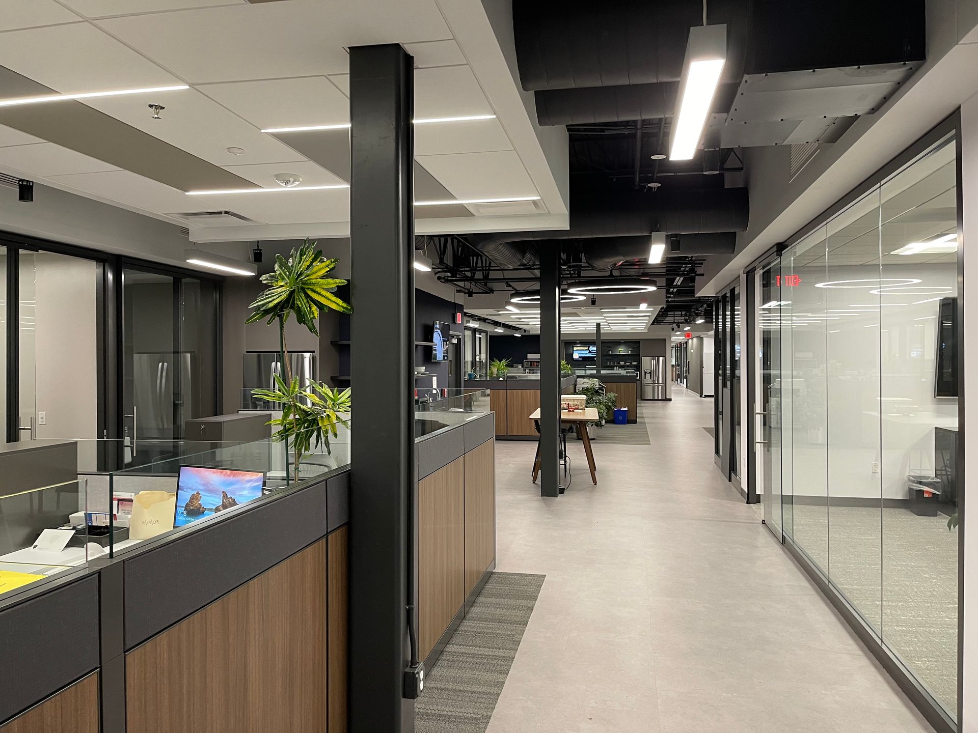 Office interior with cubicles, glass walls, and a long hallway.