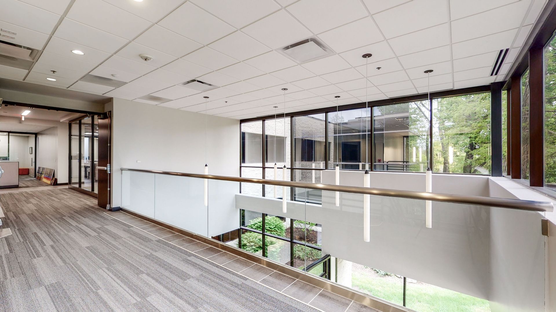 Interior office hallway with glass railings and large windows overlooking greenery.