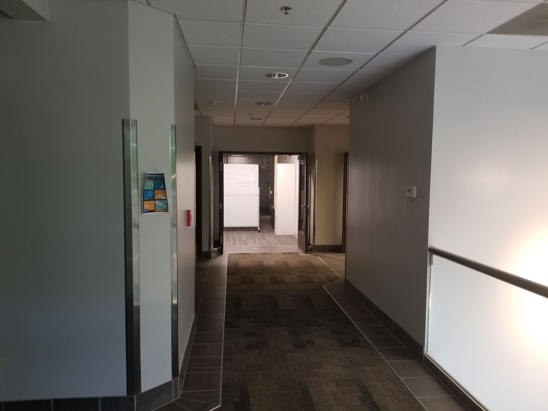 Narrow hallway with doors on either side, carpeted floor, and neutral-colored walls.