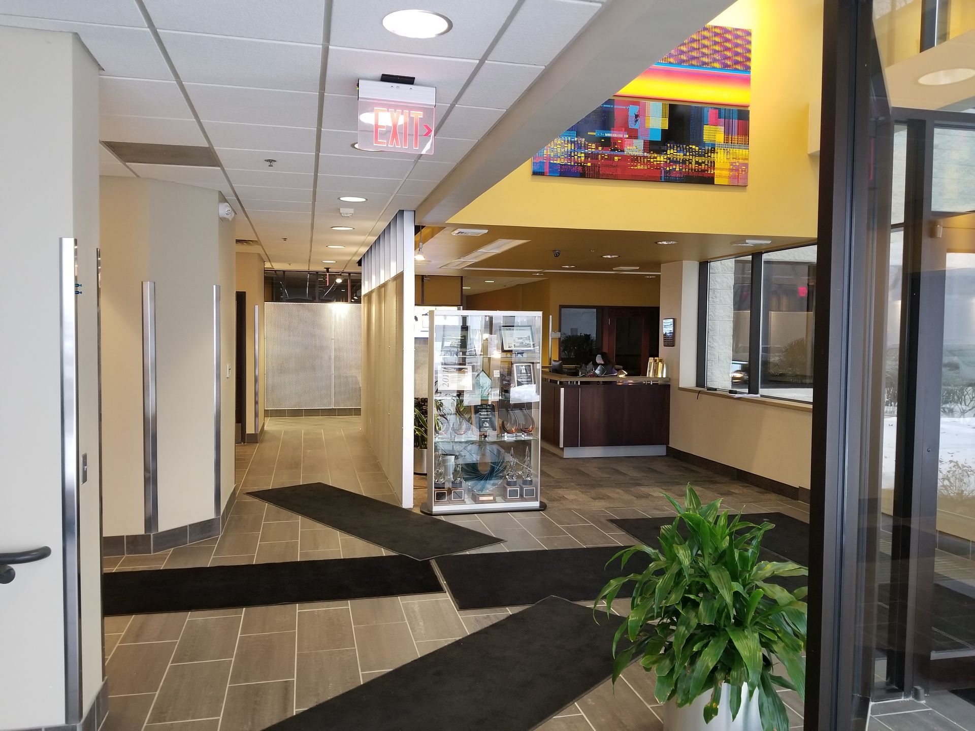 Hallway with office reception desk, artwork, and potted plant.