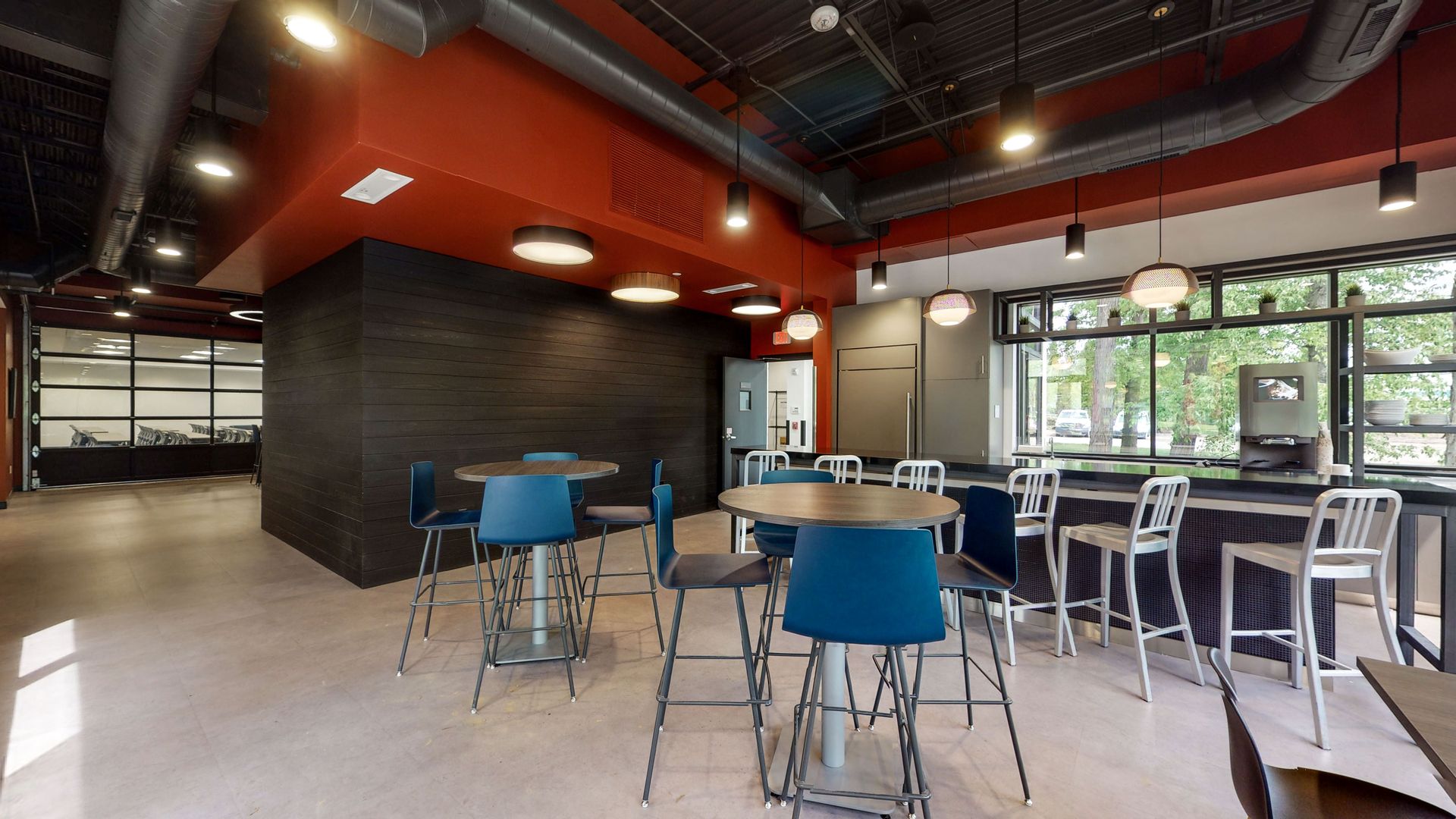 Cafe with high-top tables and stools. Red and black accents. Large windows with outside view.