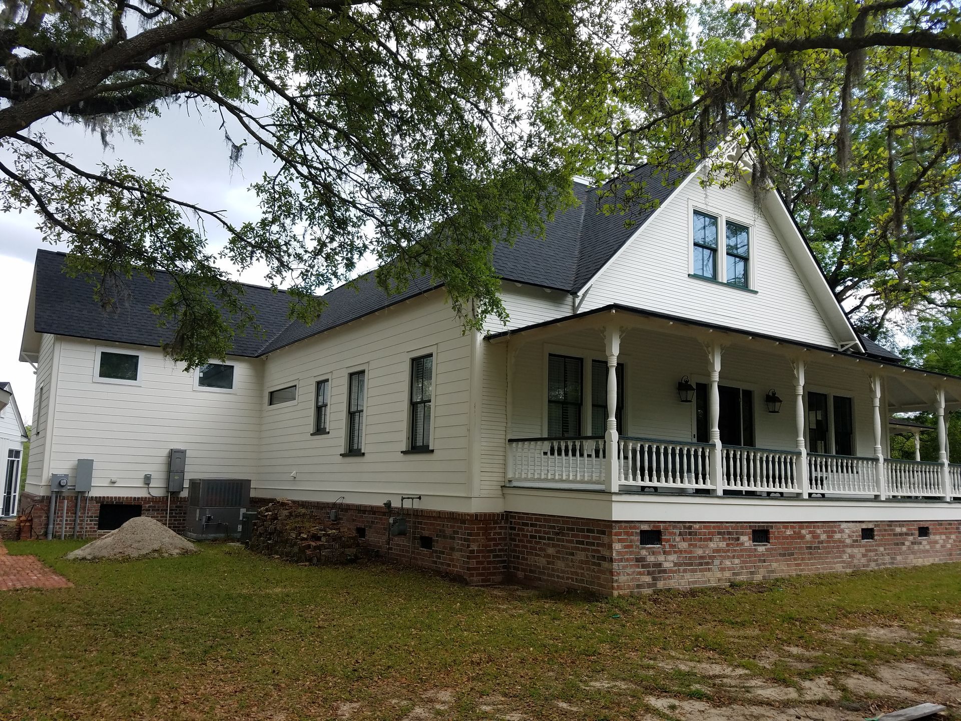 White farmhouse with a wraparound porch and dark roof, framed by trees and green grass.
