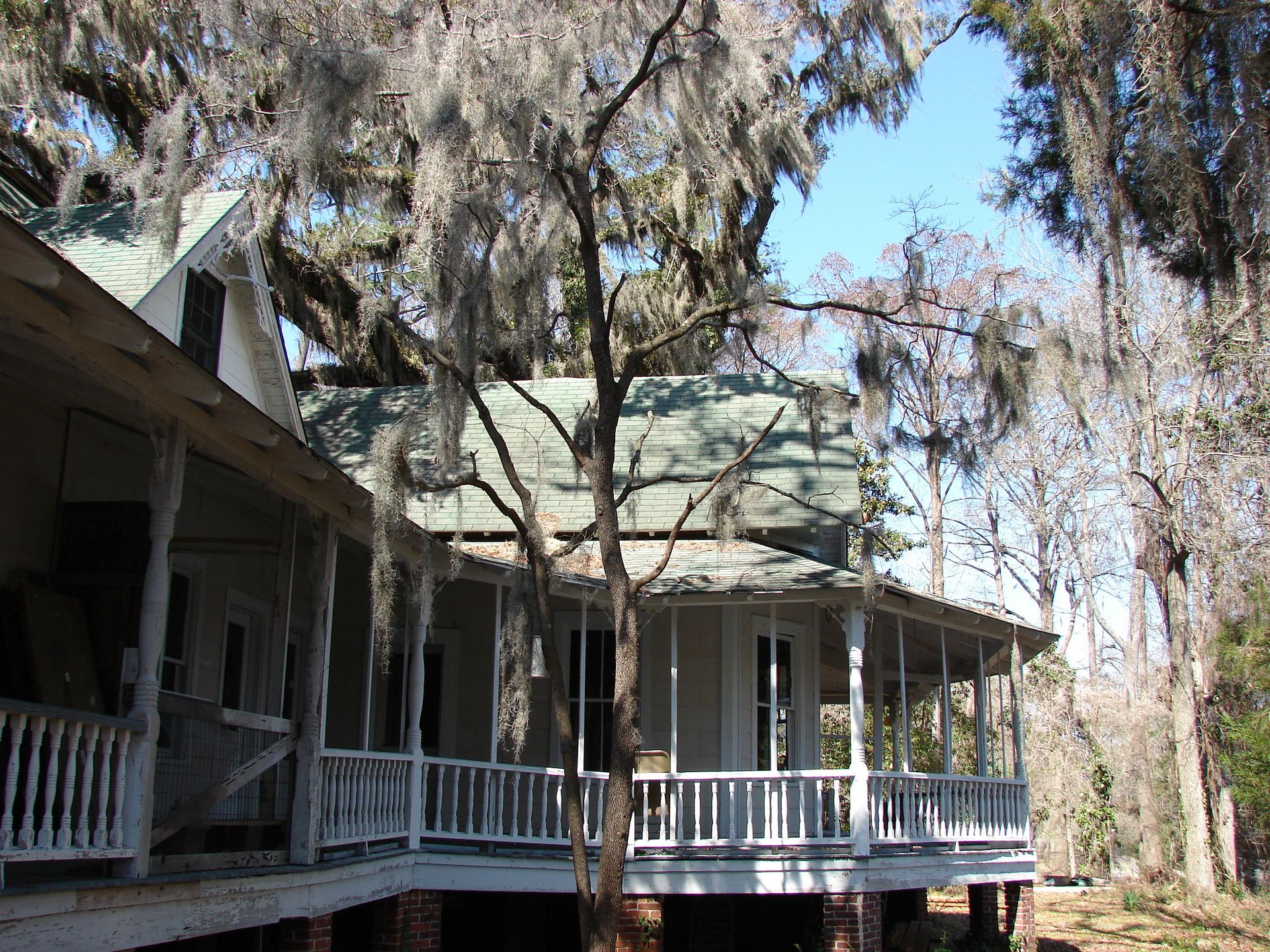 A two-story house with a porch, surrounded by trees with Spanish moss; sunny day.