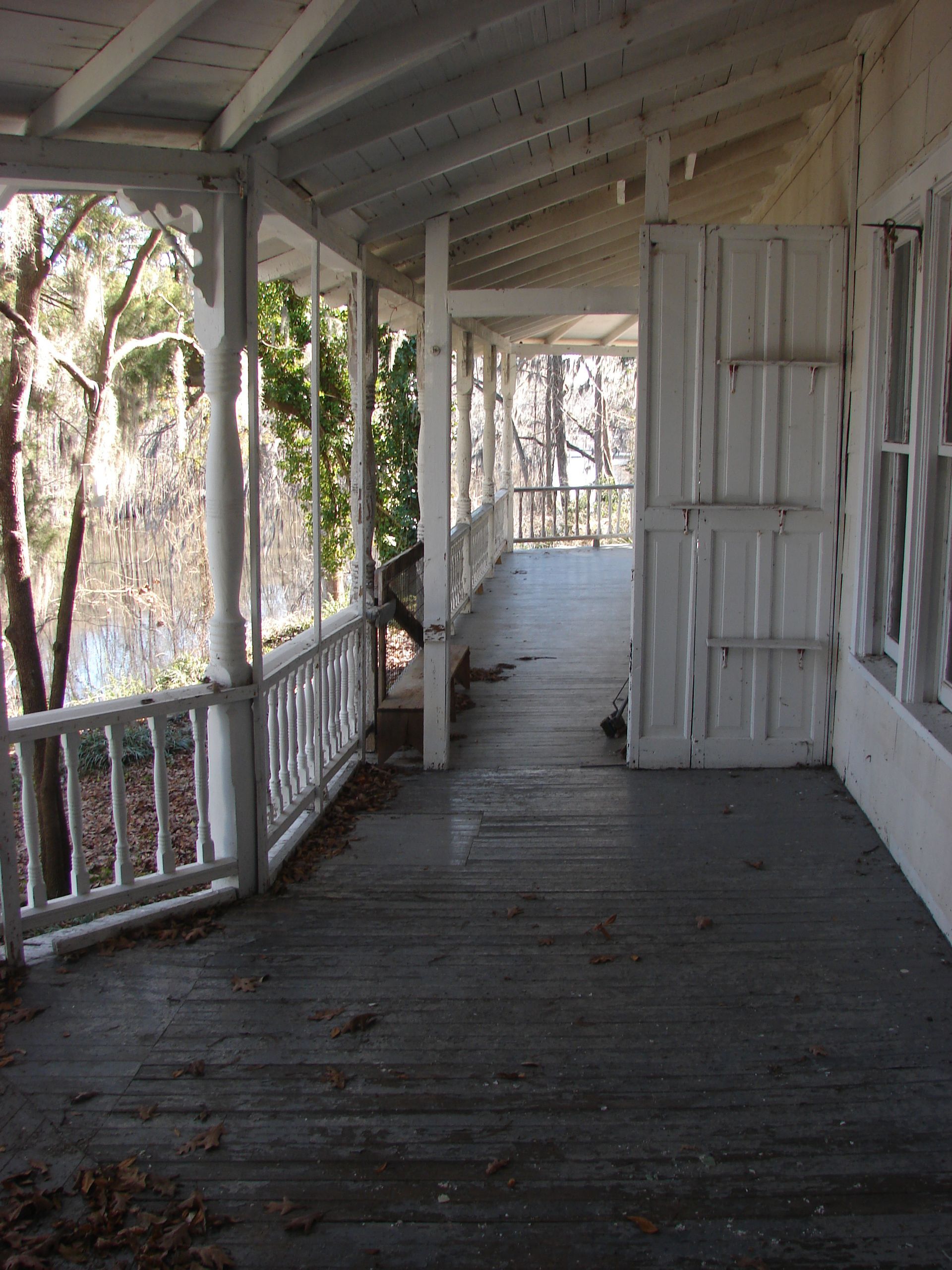 White porch with weathered gray floorboards and railing, overlooking a body of water.