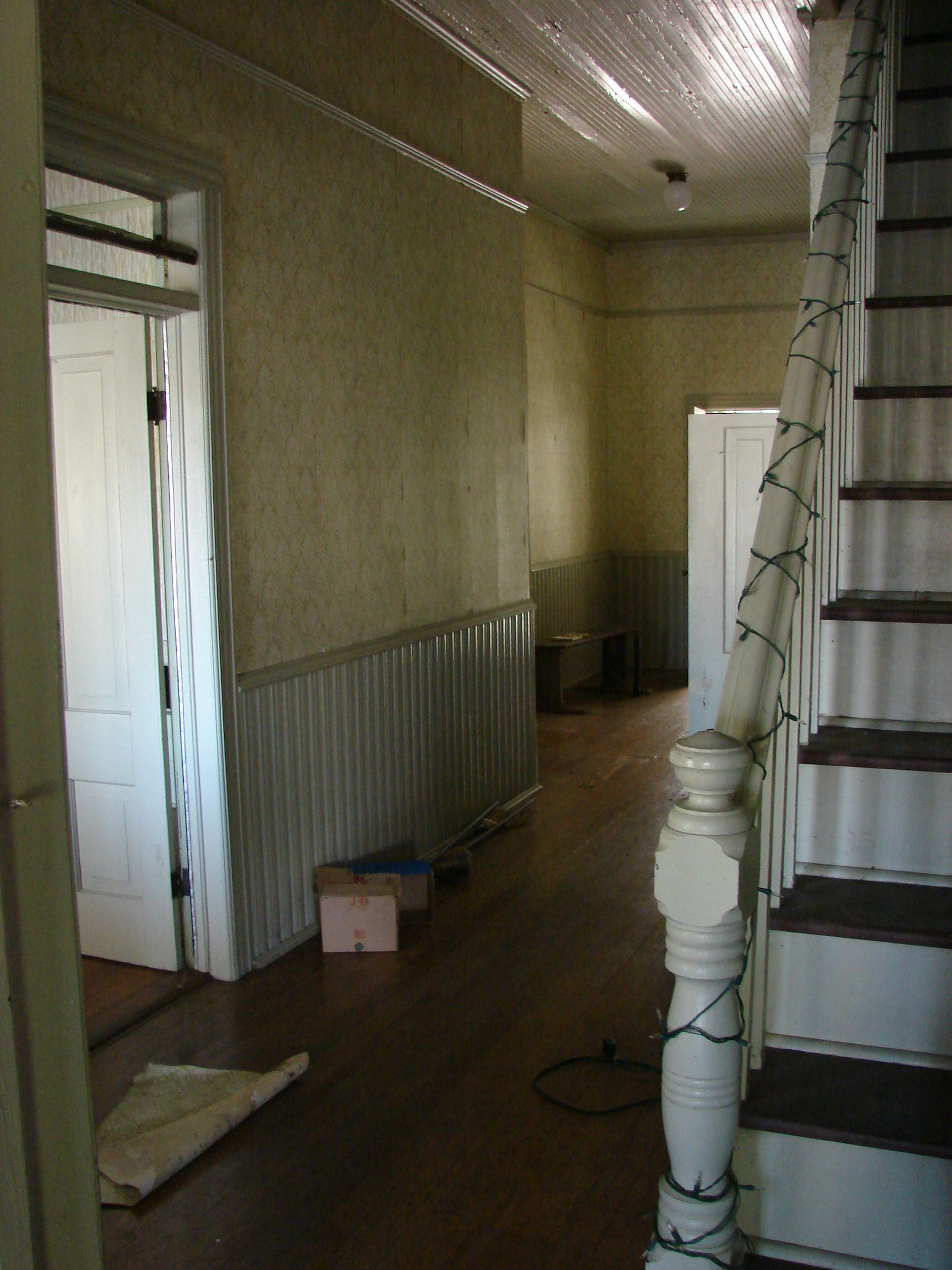 Hallway with stairs, wood floors, paneling, and doorways; decorated with string lights.