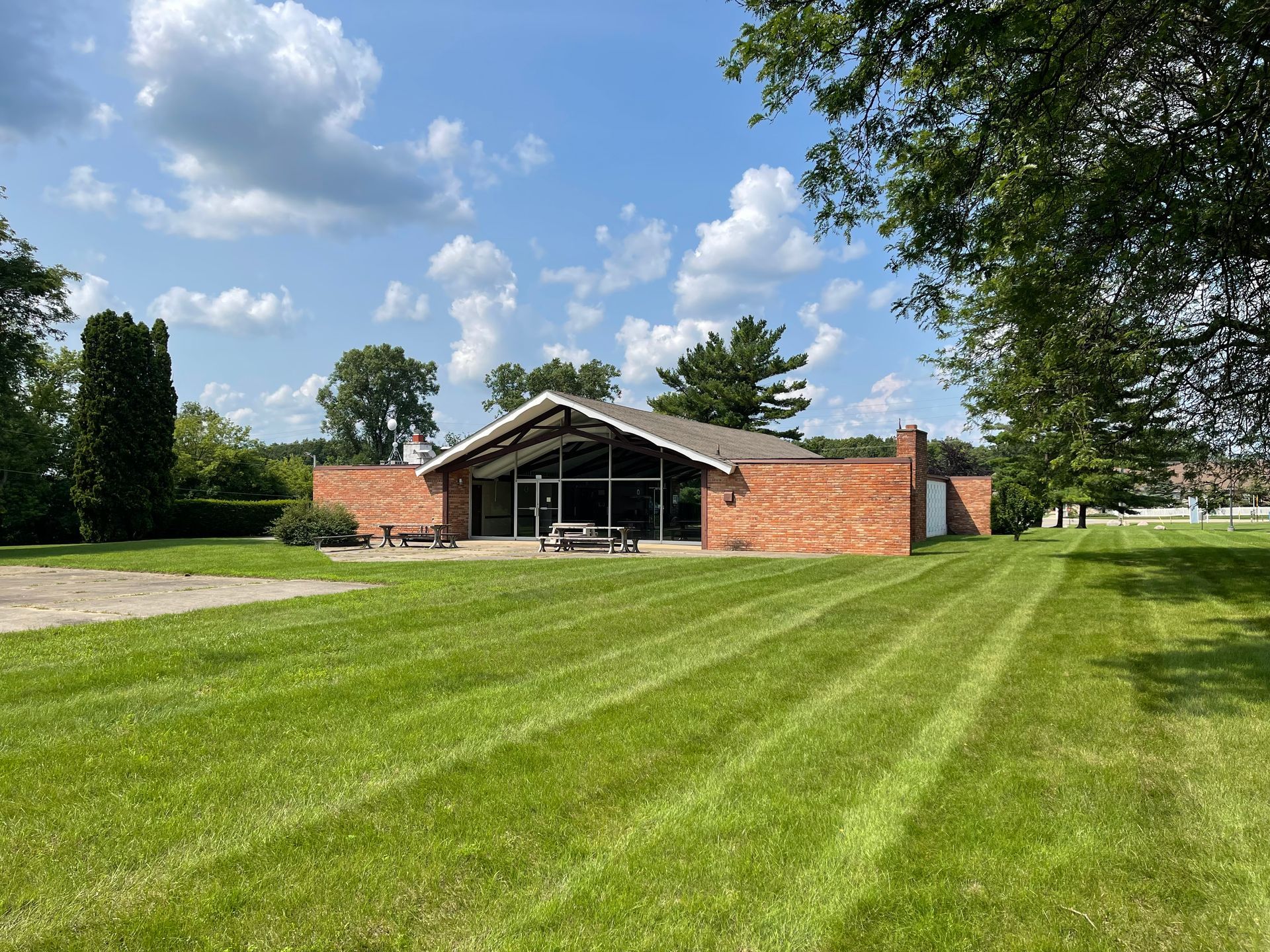 Red brick building with large glass front and pitched roof, set on a well-mowed lawn under a blue sky.