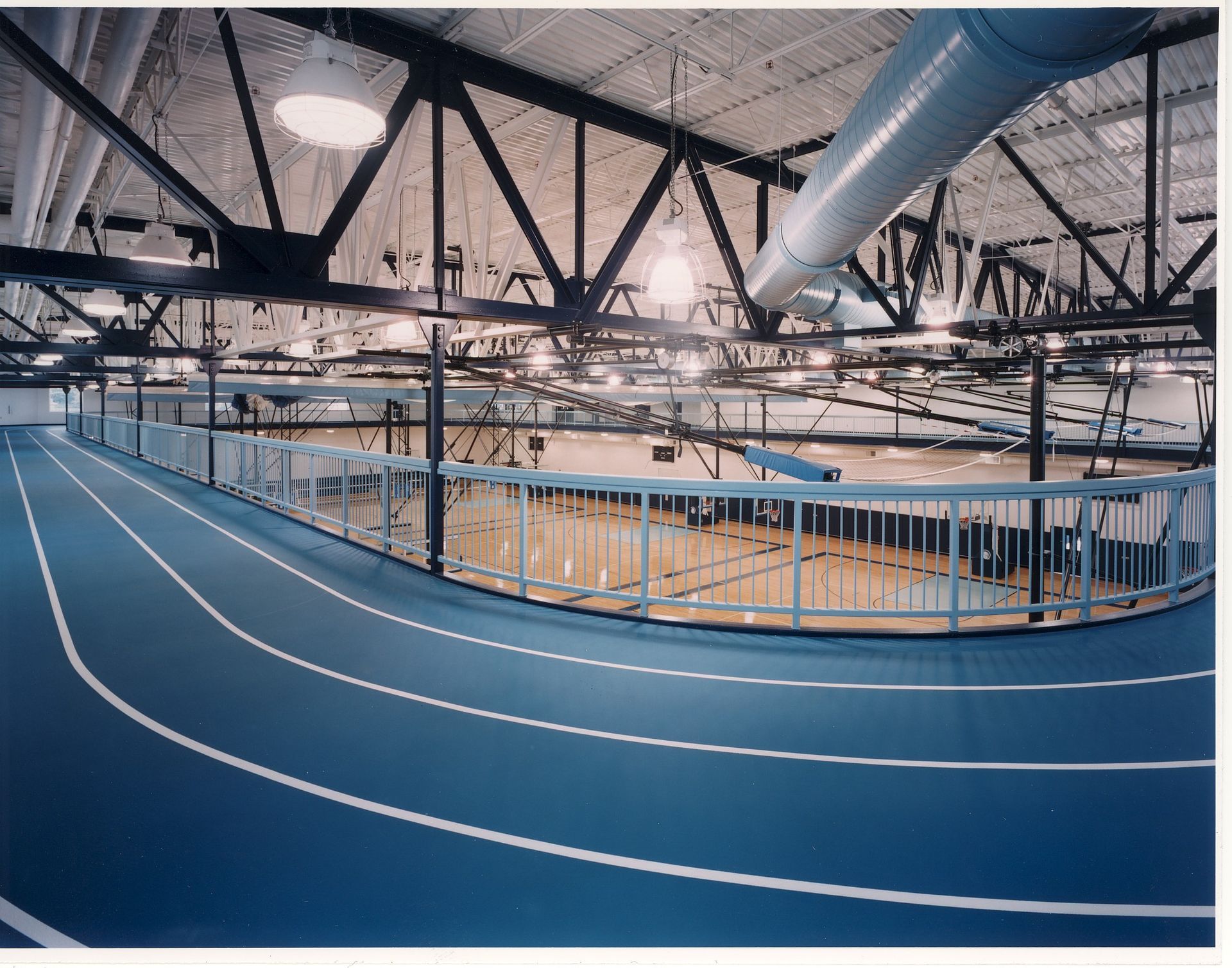 Blue indoor running track circling a basketball court. Black steel beams and bright lights.