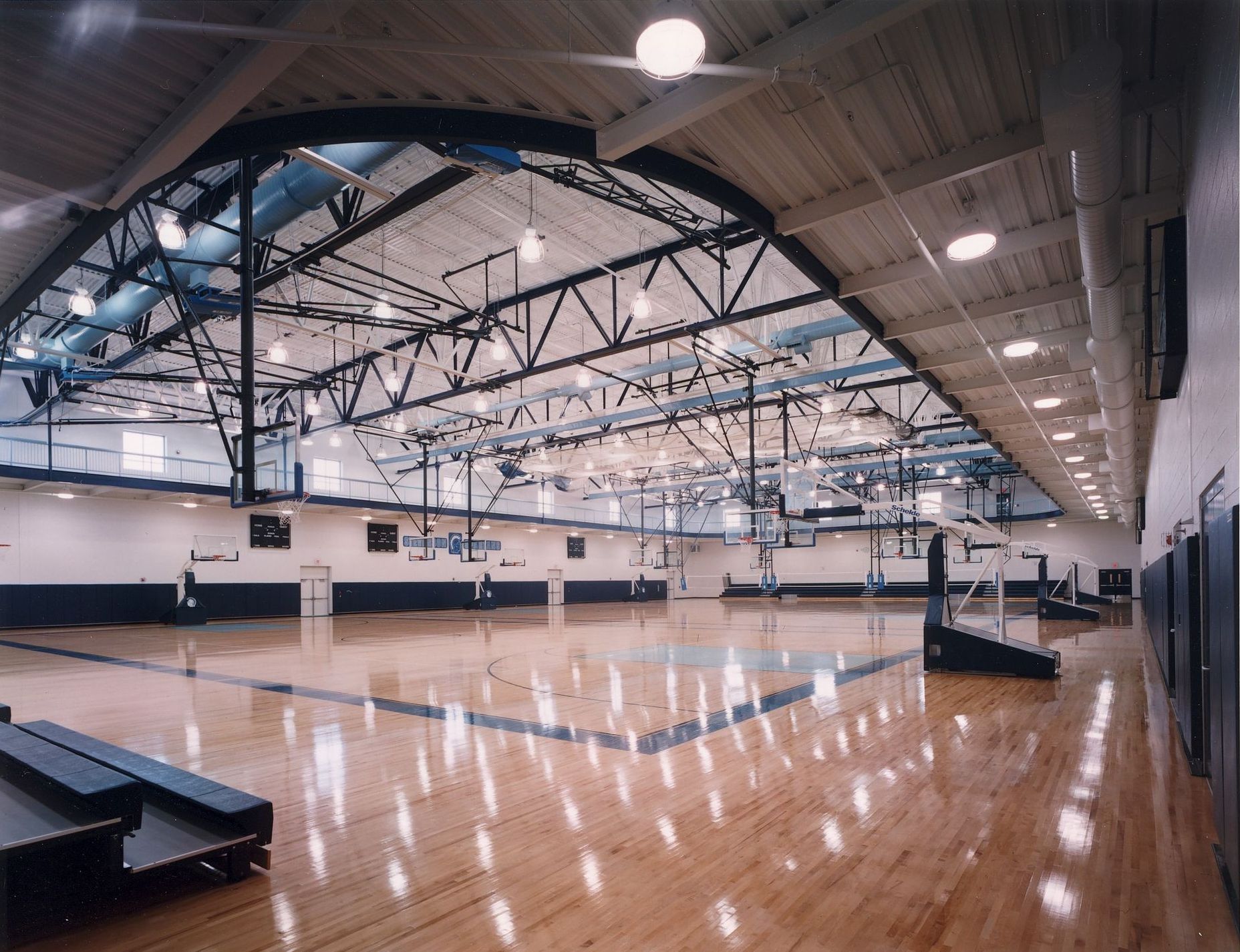 Gymnasium interior, wood floor, basketball hoops, ceiling lights, steel trusses.