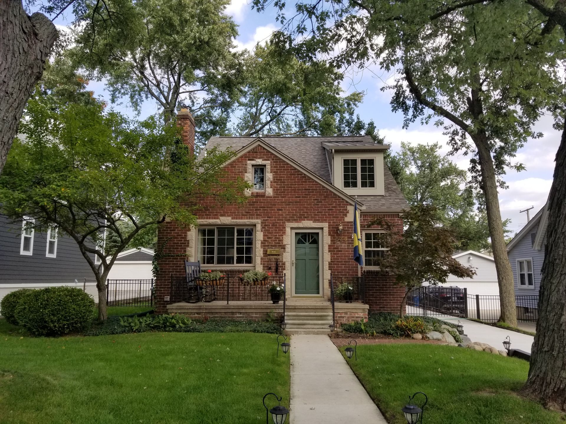 Brick house with green door, brown roof, and small front yard, trees on either side.
