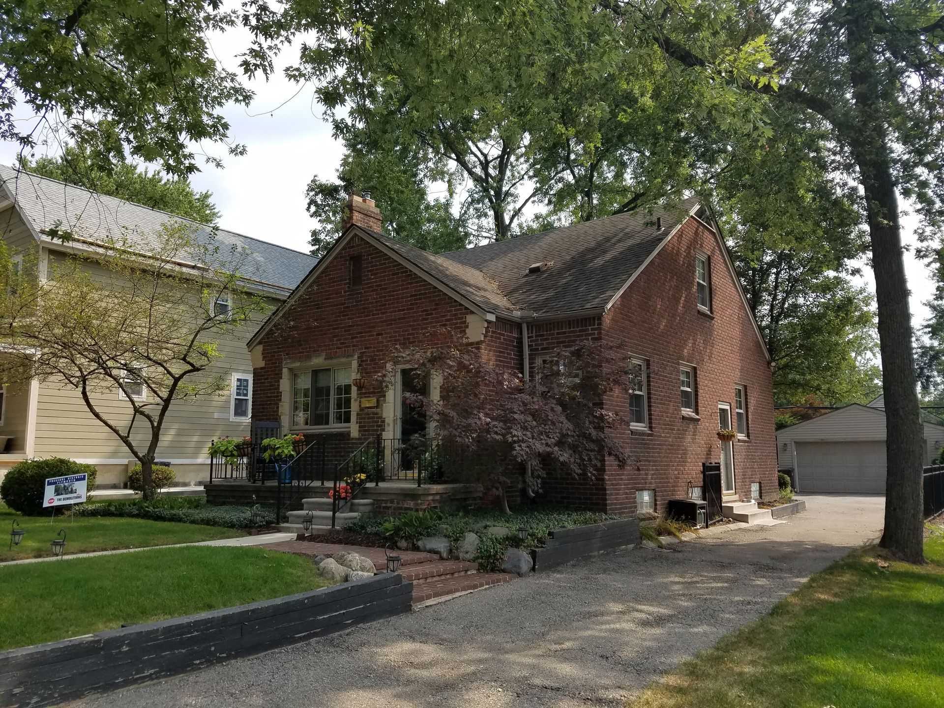 Brick house with ivy, green lawn, and gravel driveway. A neighboring house is visible to the left.