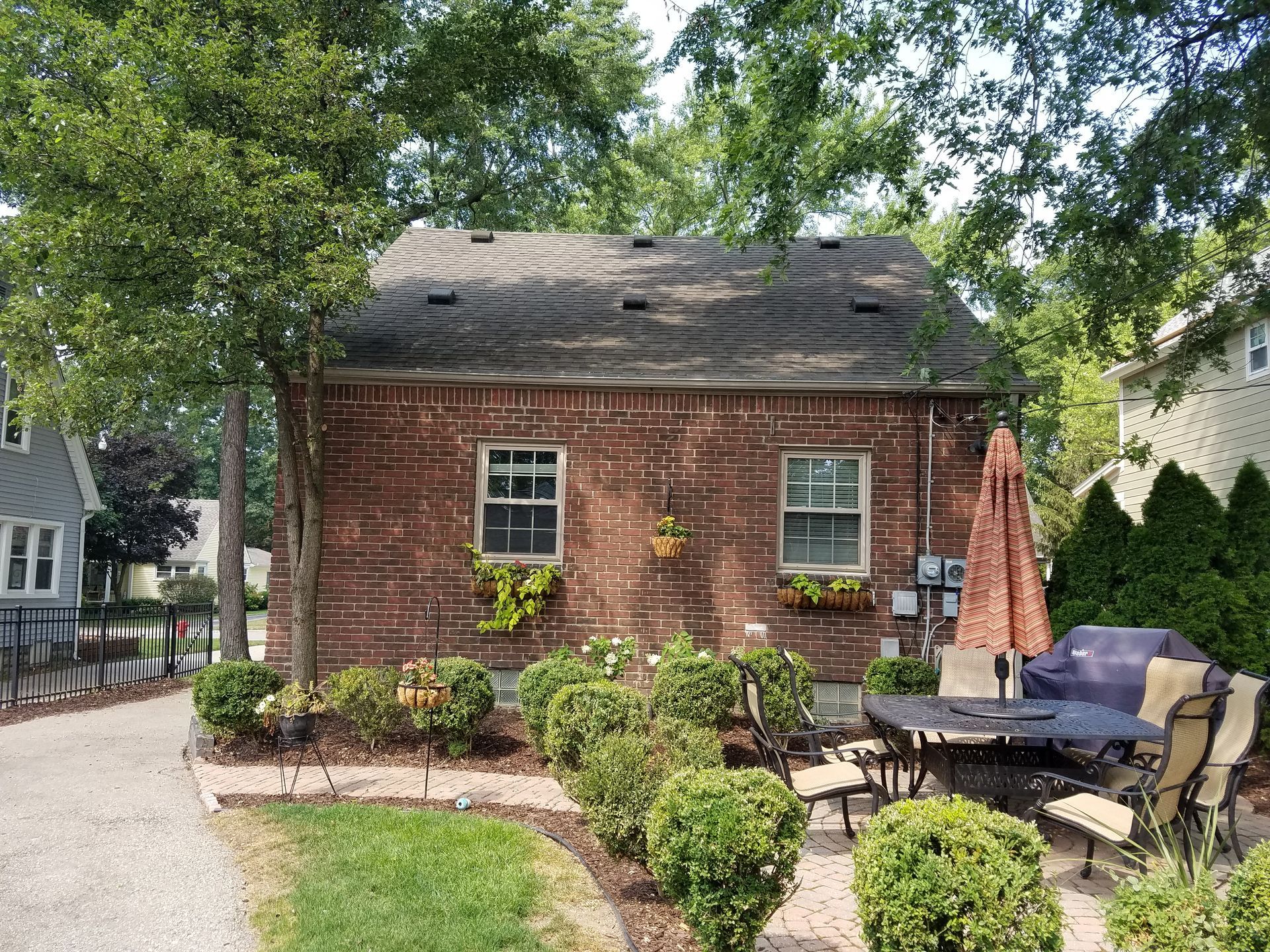 Brick building with windows and flower boxes, a patio with furniture, and a landscaped garden.