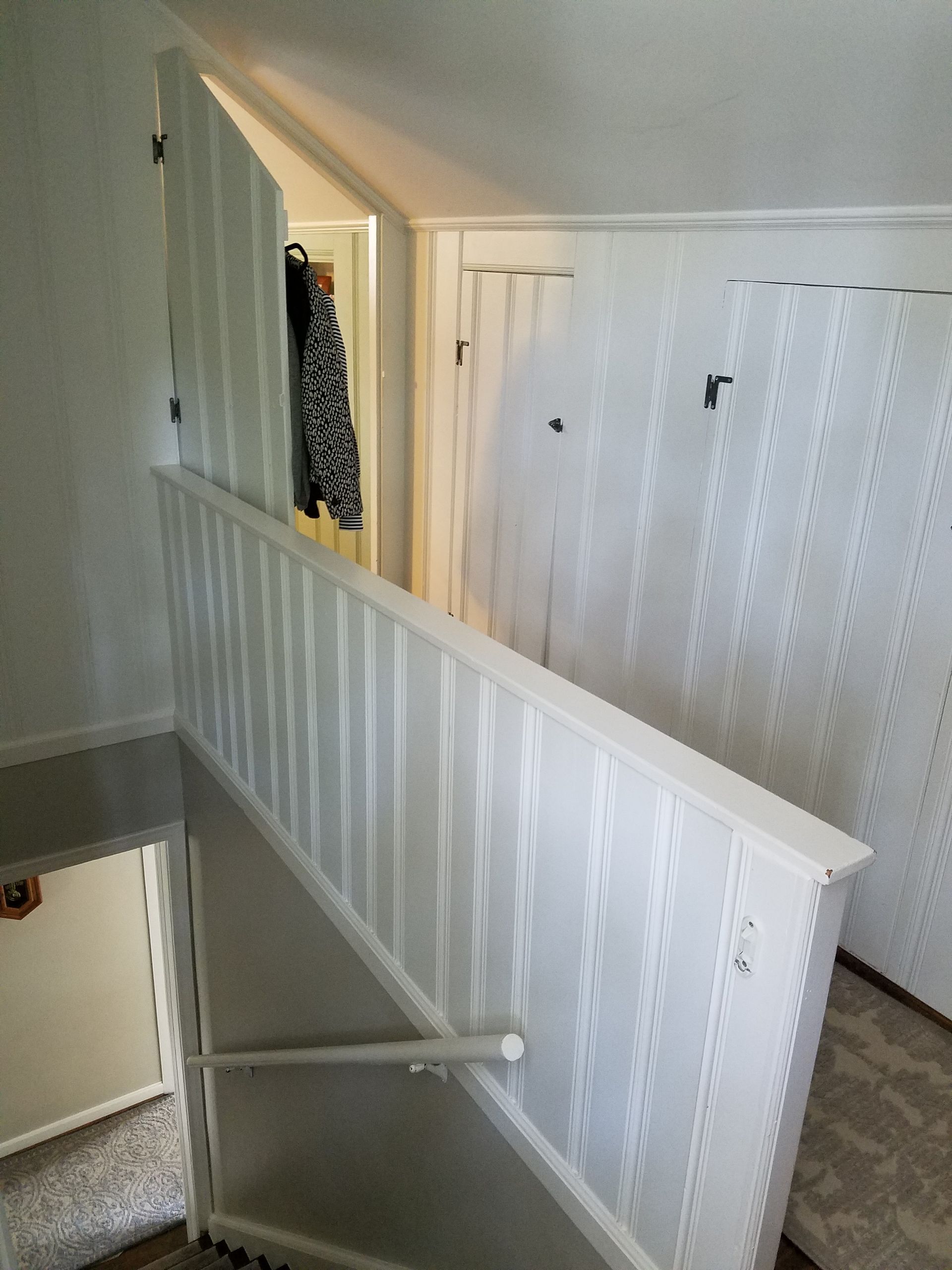 Interior view of a stairway with white paneling, handrail, and doorway, featuring coat hanging.