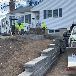 Workers laying green sod in a narrow courtyard between brick apartment buildings.