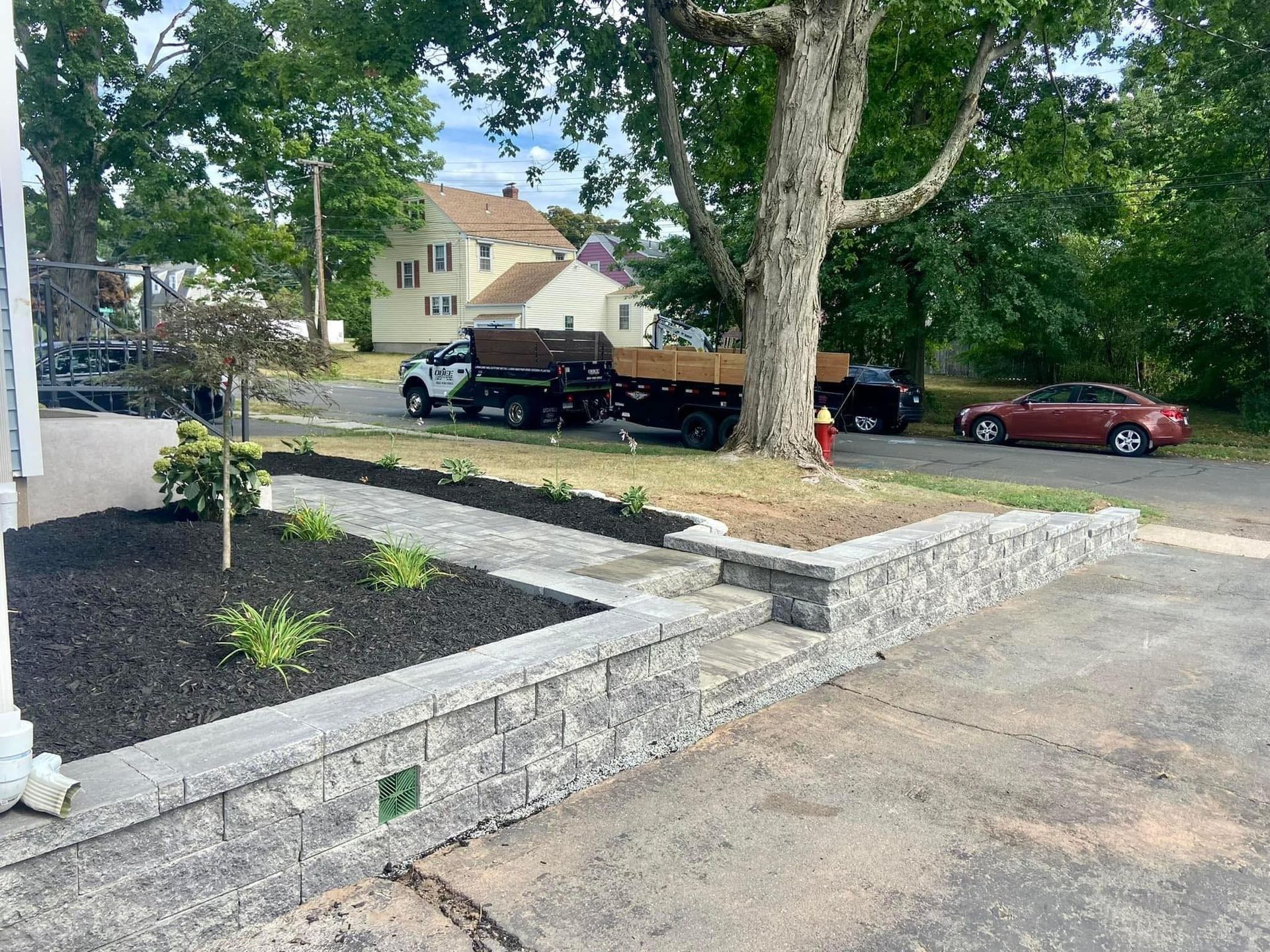 Stone retaining wall and landscaped parking lot with trees, trucks, and a red car in the background
