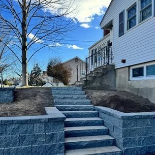 Stone steps and retaining walls leading up a sloped front yard beside a white house under a blue sky