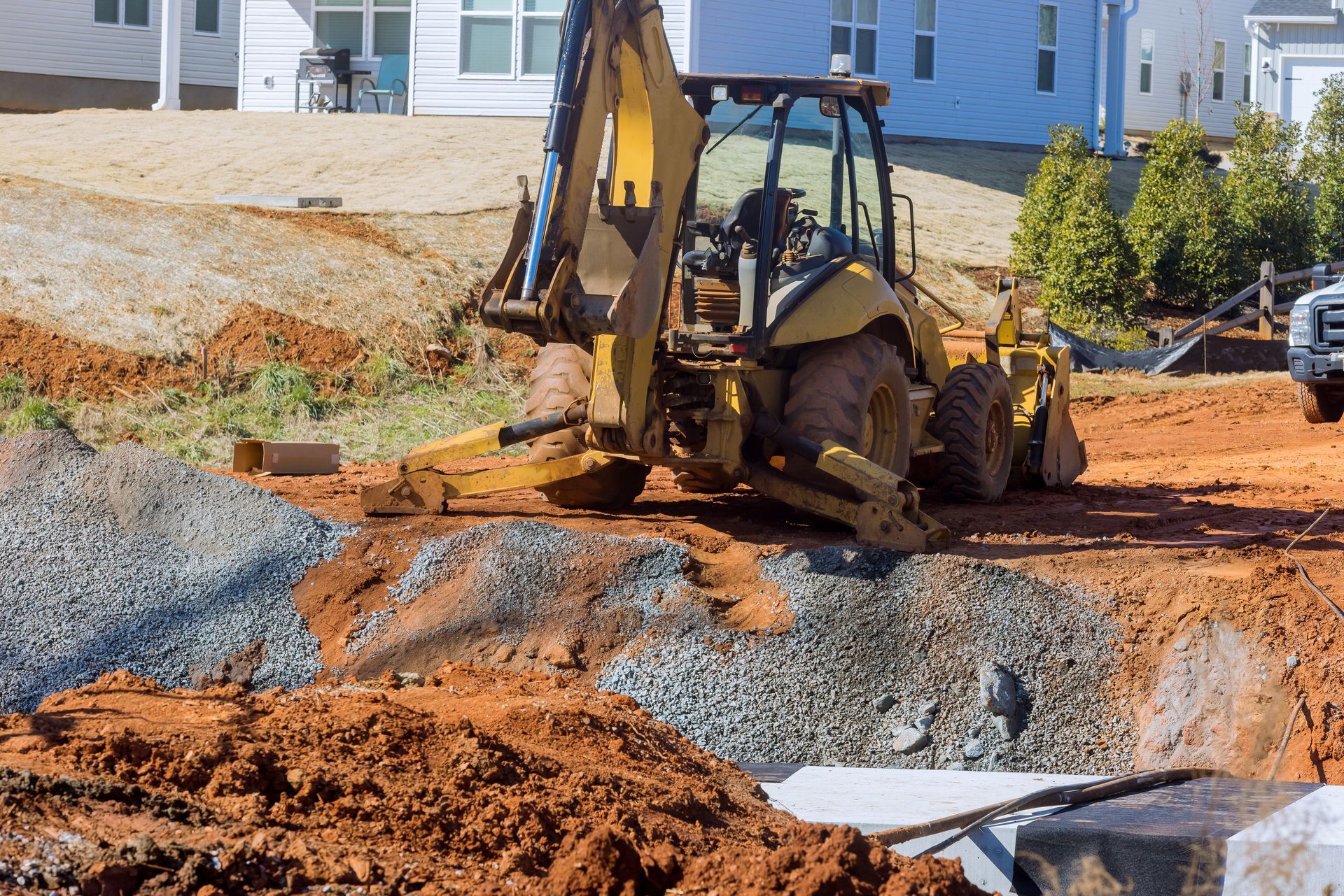 Backhoe excavator digging soil at a construction site beside homes