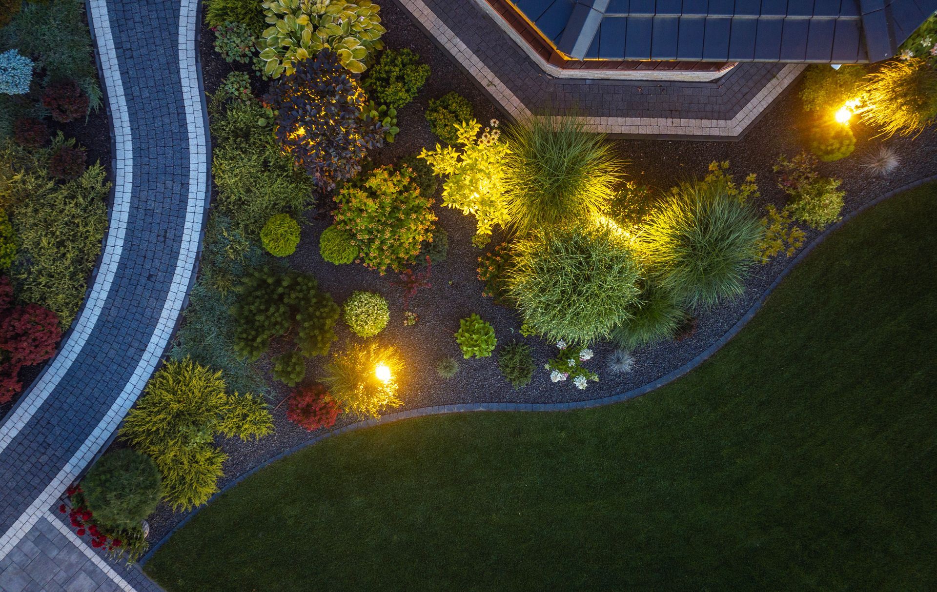 Overhead view of a landscaped garden with glowing lights beside a building and curved walkway
