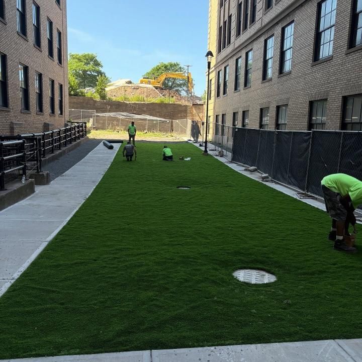 Workers installing grass in a narrow courtyard between brick buildings.